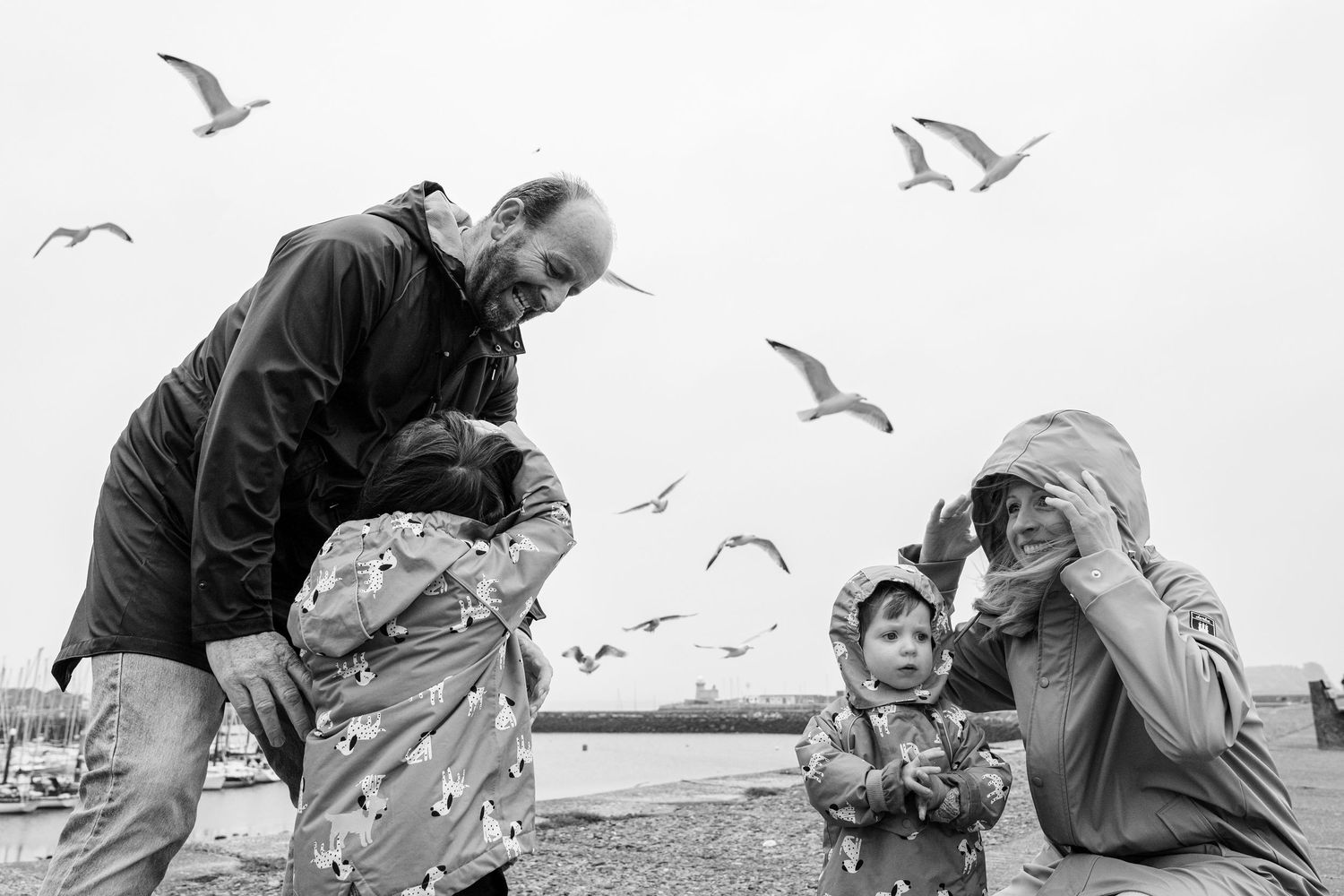 Black and white photo of a family surrounded by seagulls on a seaside pier. PHOTOGRAPHER Dublin