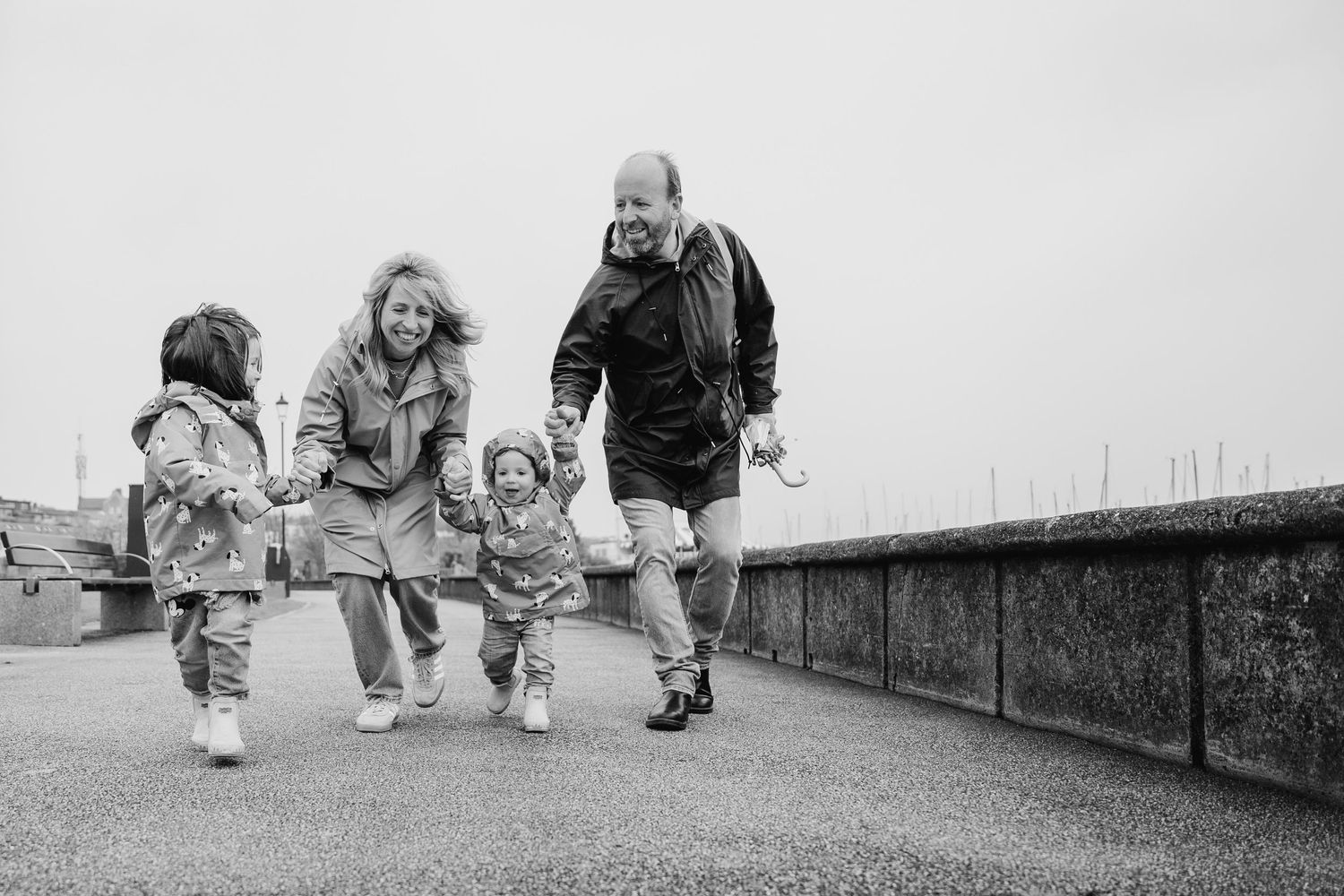 A group in winter coats enjoys a playful walk along a stone wall path in black and white. PHOTOGRAPHER Dublin