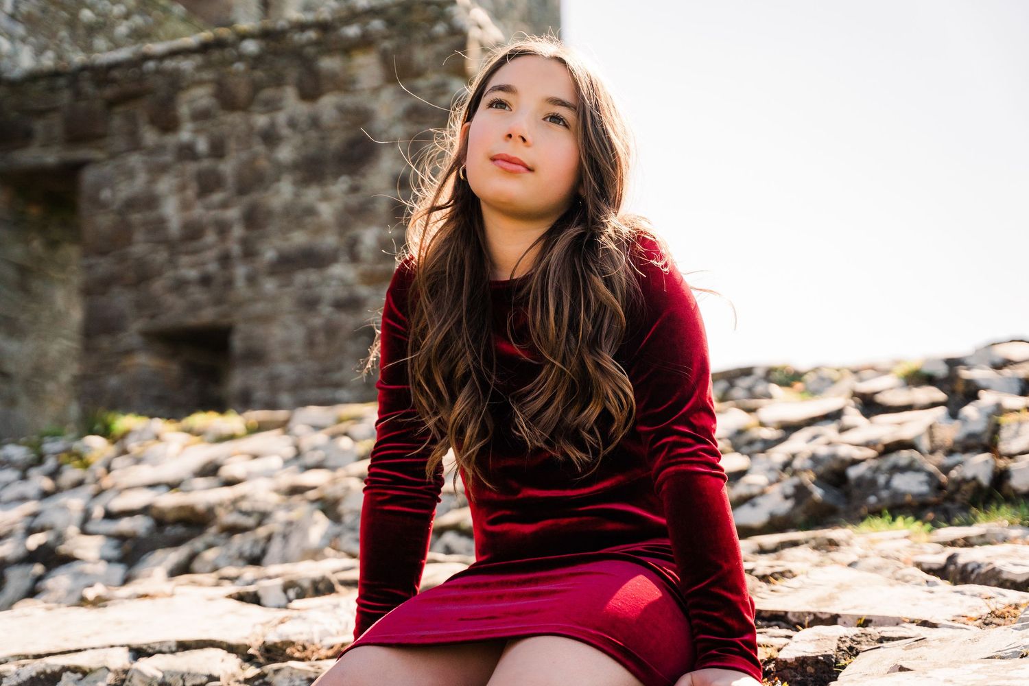 A red velvet dress stands out against rocky ruins in warm sunlight. Family PHOTOGRAPHER Dublin