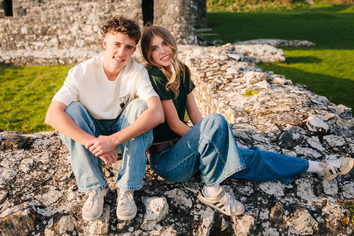 A couple sits casually on stone wall outdoors enjoying sunset lighting during a summer photoshoot. Photographer Ireland dublin