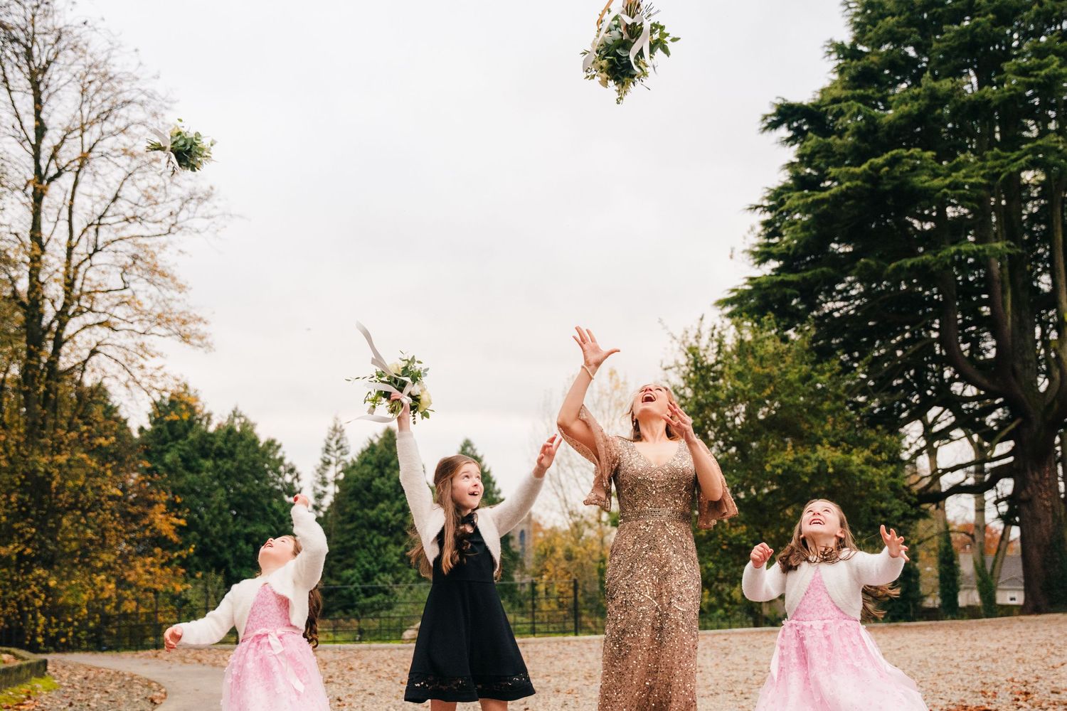 Women and children toss flower bouquets in the air during an outdoor celebration. Wedding Photographer Dublin Ireland