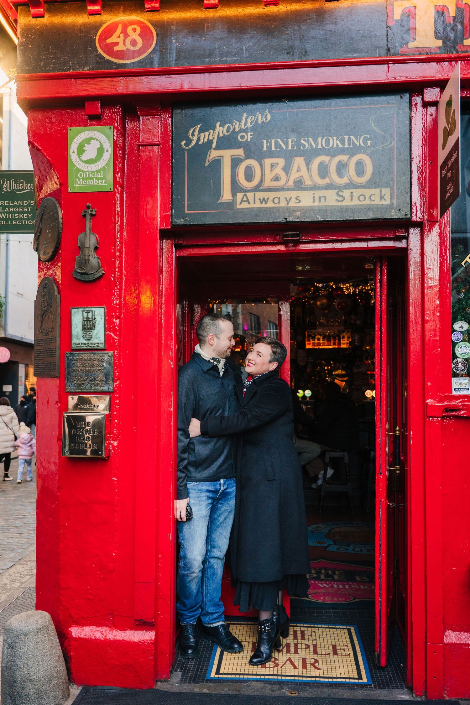 Bright red storefront of a tobacco shop with customers gathered outside during the holiday season. Family walking through Dublin city centre