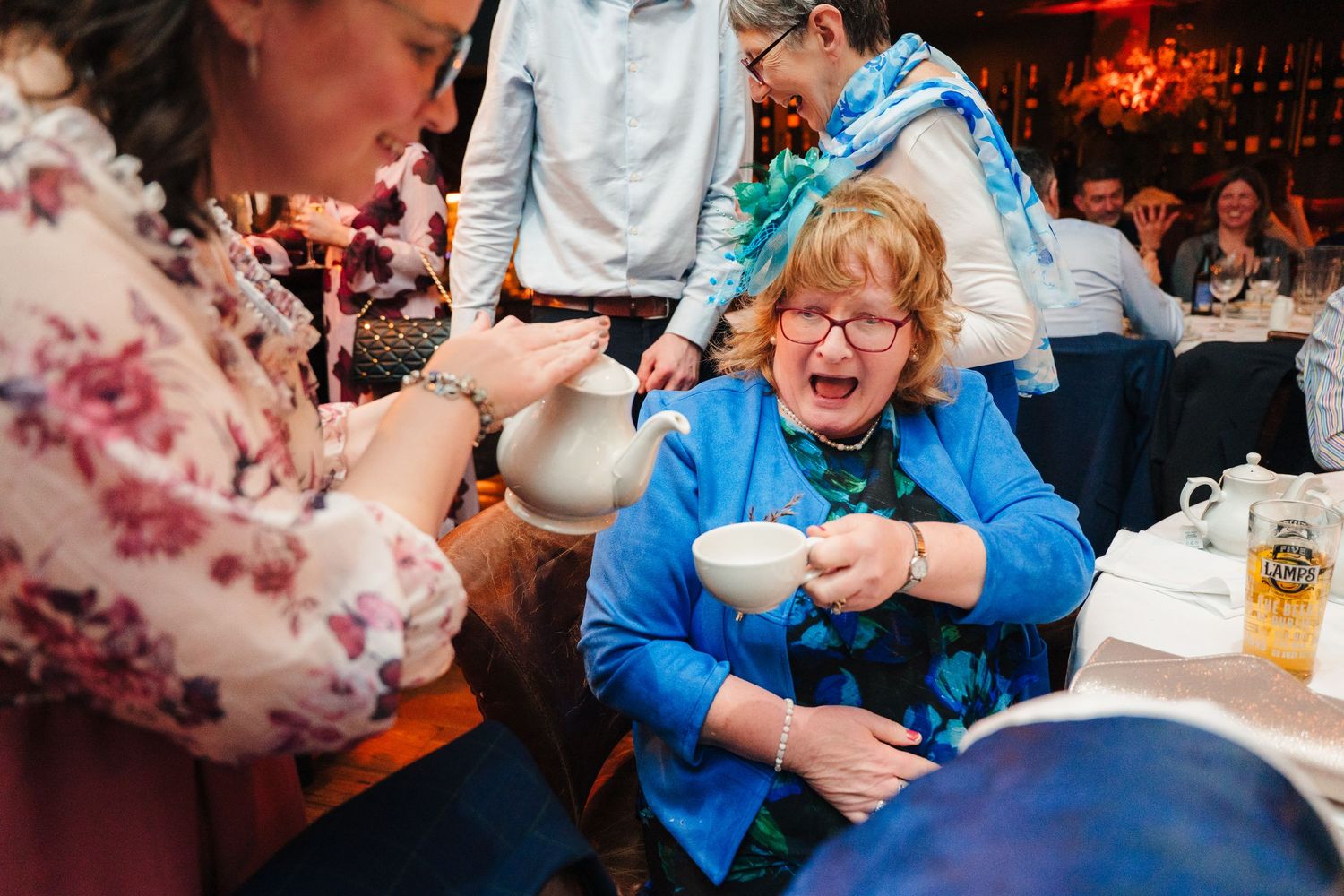 Guests laughing and enjoying drinks during an animated wedding reception celebration. Wedding photographer dublin