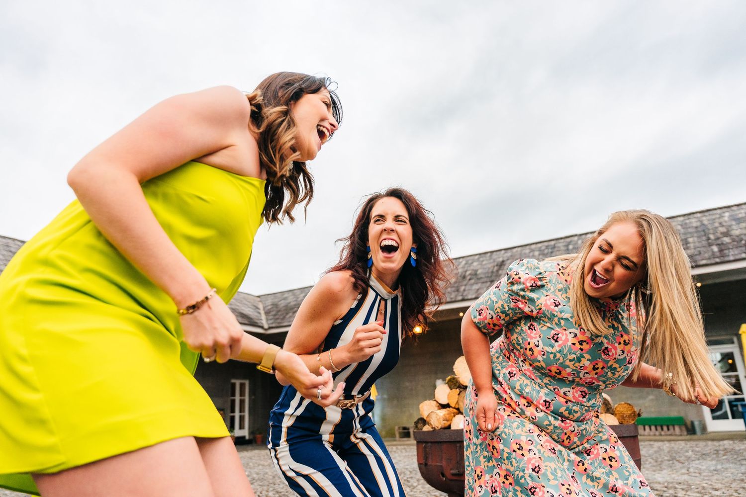 Three friends dancing and laughing together outdoors in colorful summer dresses. wedding photographer dublin pricing meath