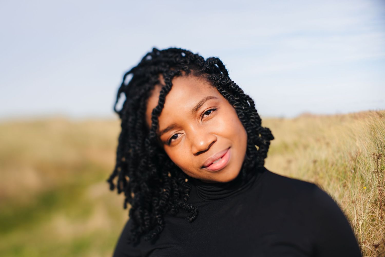 Person in black turtleneck smiling warmly against blurred coastal background. Dublin professional headshots photographer