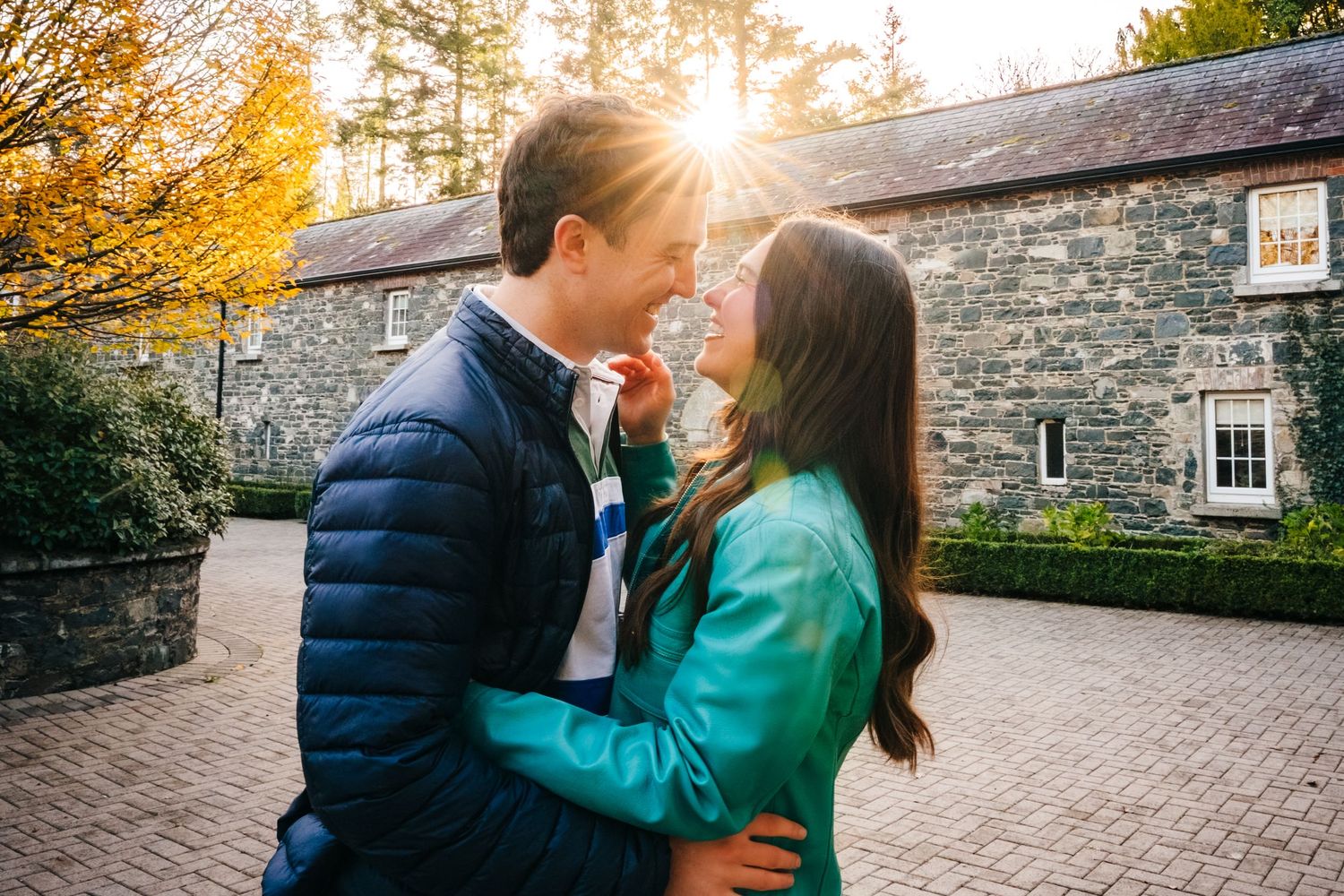 A romantic couple embraces during golden hour in front of a rustic stone building in autumn. engagement photographer dublin