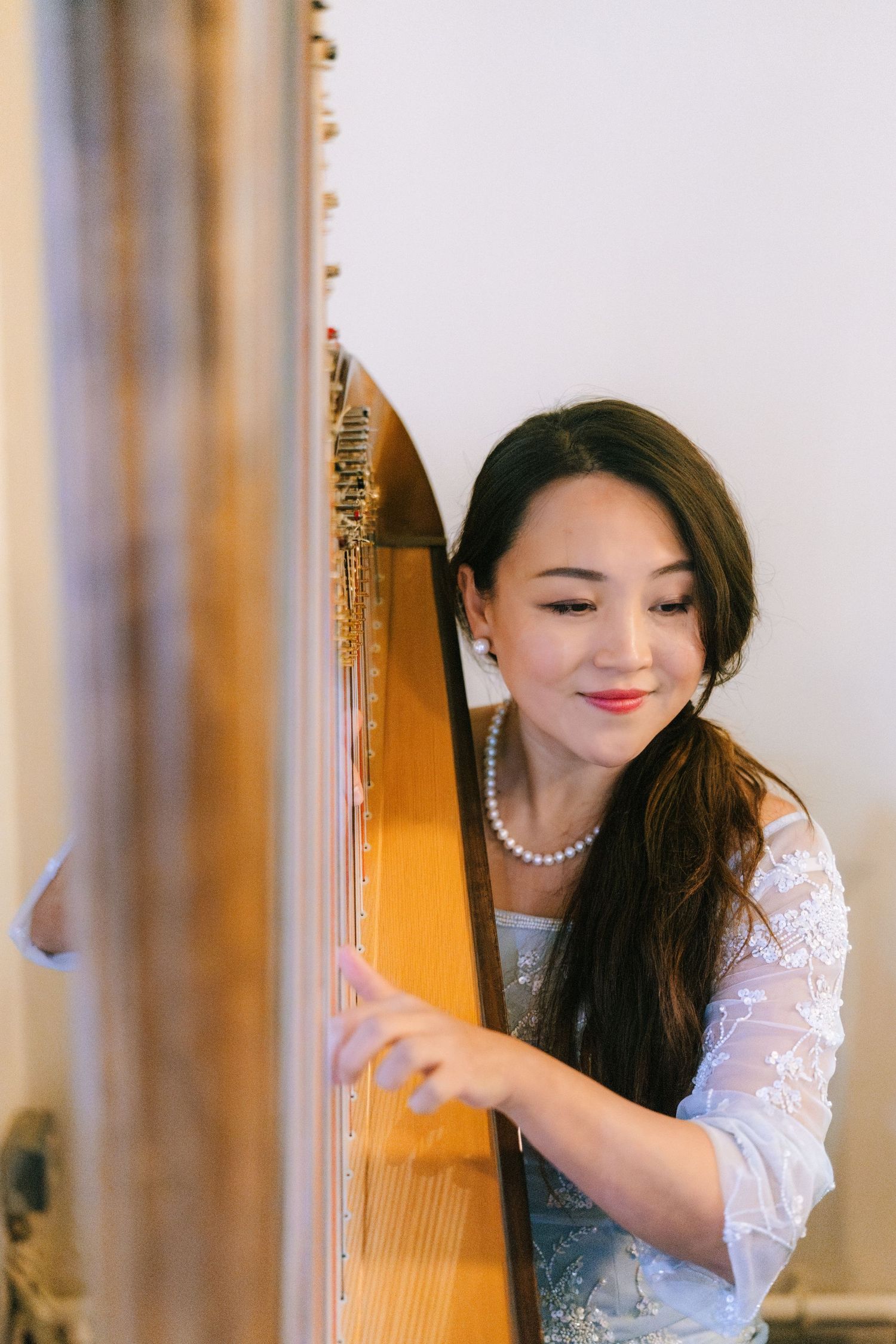 A musician in white lace and pearls plays a golden harp in an elegant setting.