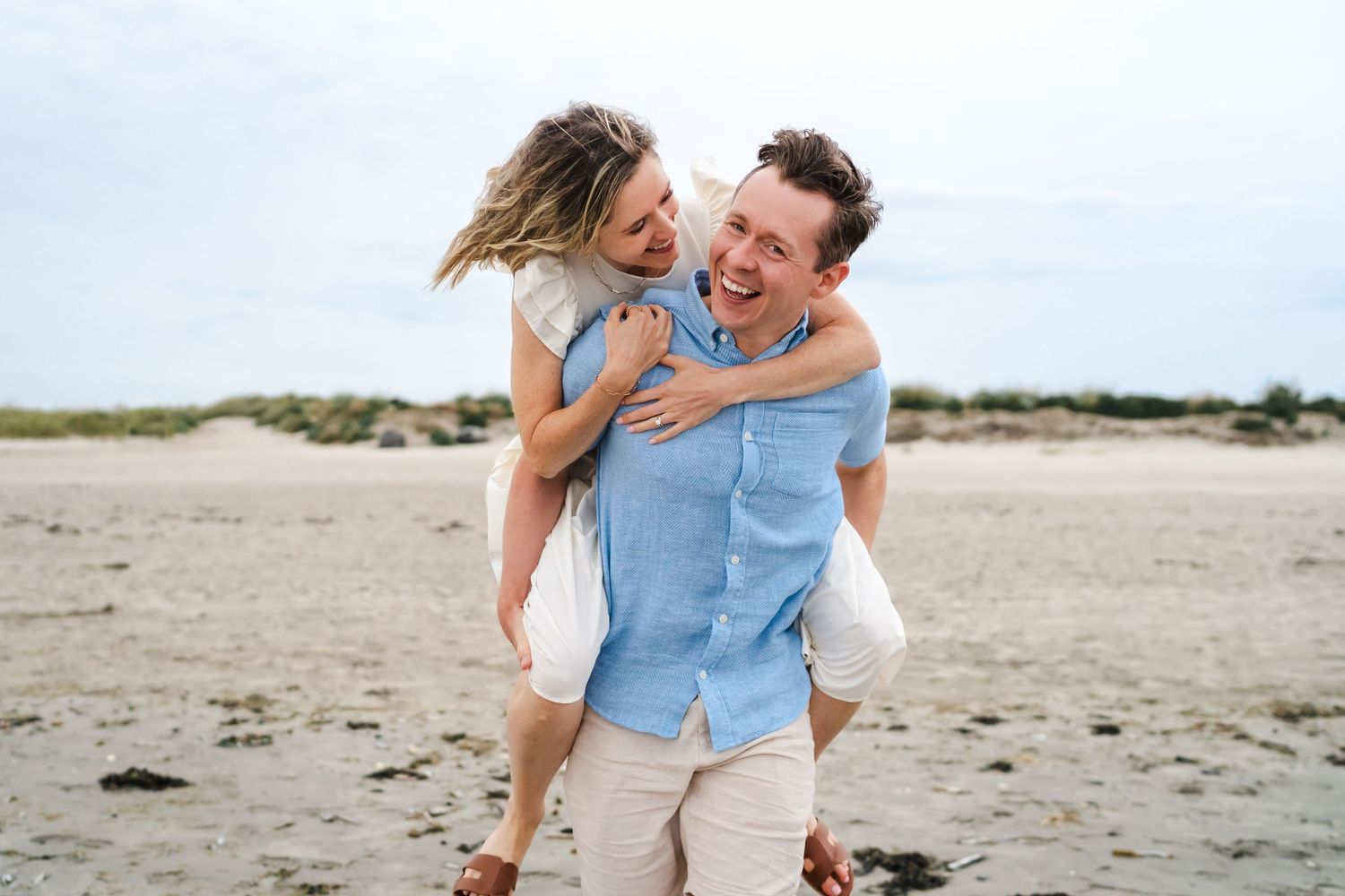 Happy couple sharing playful moment while running on beach with ocean in background.  Family photographer Dublin Ireland