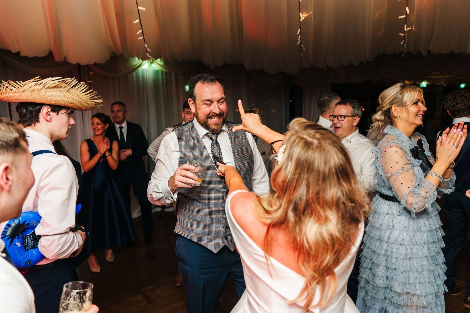 Lively dance floor scene with wedding guests dancing and celebrating under tent lighting.  Virginia Park Lodge Wedding Photographer Cavan Du