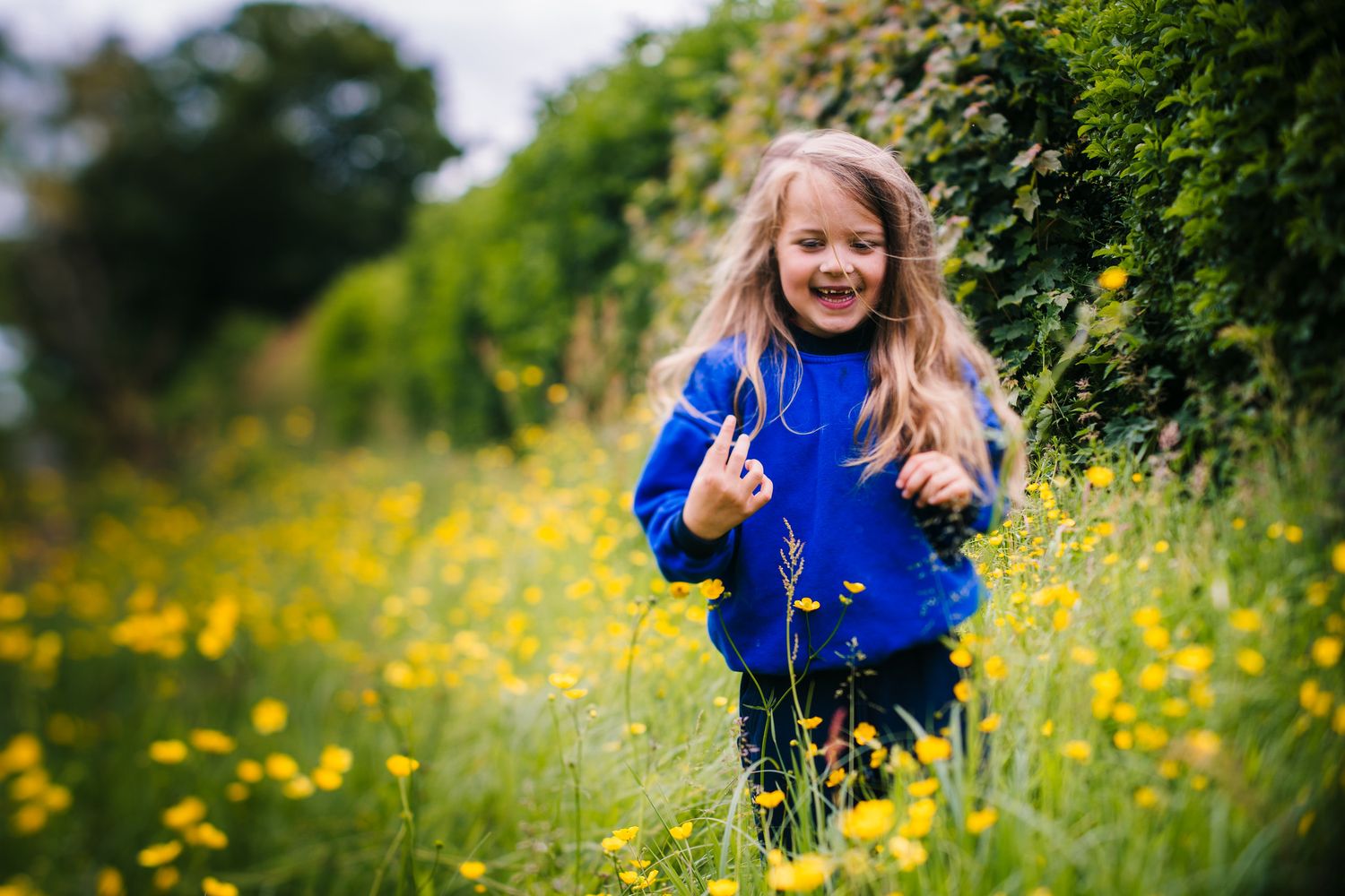 A child in a bright blue sweater runs joyfully through a meadow filled with yellow wildflowers on a sunny day. Family PHOTOGRAPHER Dublin