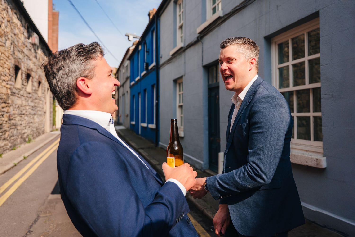 Friends sharing jovial moment on urban street with blue window frames. Same sex wedding PHOTOGRAPHER Dublin