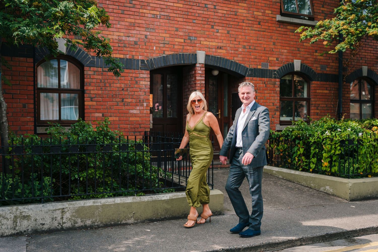 People walking along a red brick building exterior with landscaping. Same sex wedding PHOTOGRAPHER Dublin