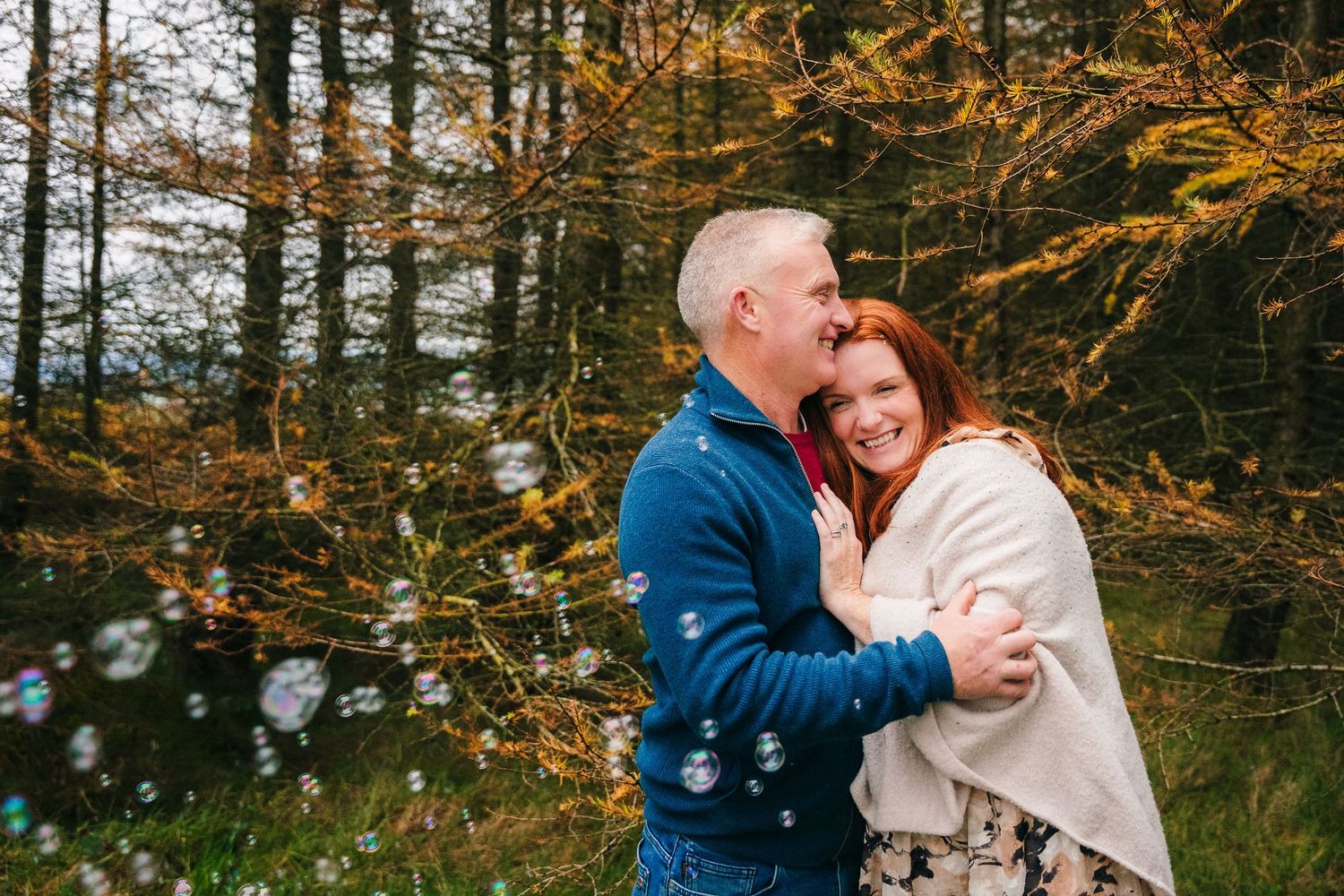 A couple embracing in a forest surrounded by golden autumn foliage.
