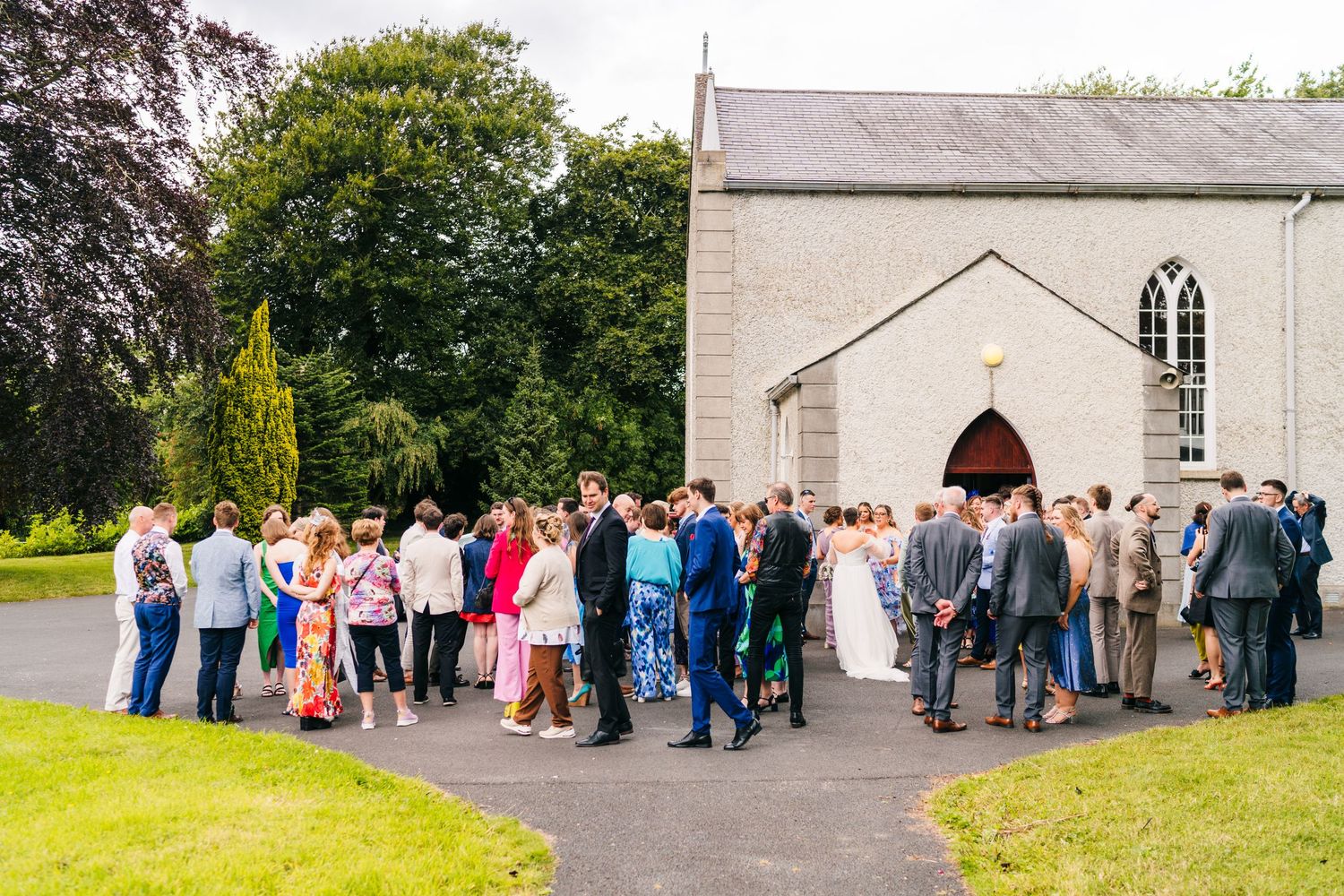 Millhouse slane wedding photographer dublin Large group of wedding guests gathered outside a traditional white stone church building.