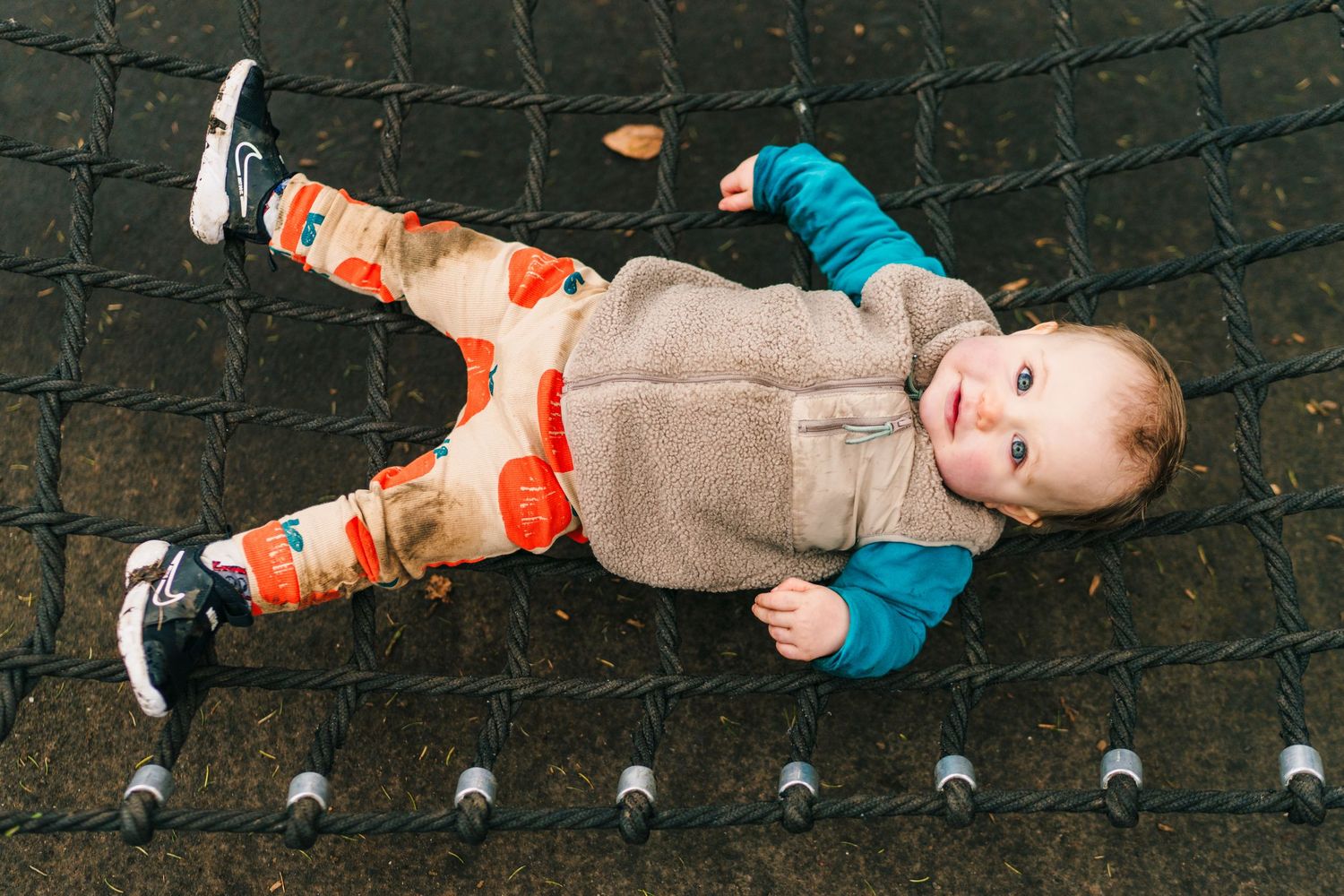 Family photographer Dublin Ireland  A small child lies playfully on a rope climbing structure at a playground.