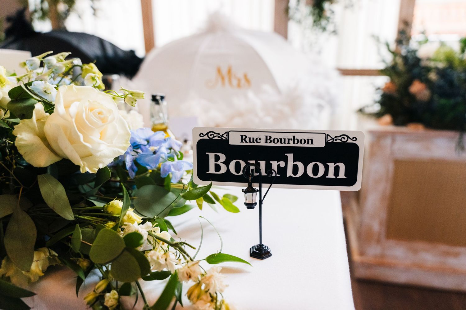 A table decoration featuring white roses and blue flowers with a Bourbon table marker. PHOTOGRAPHER Dublin Ireland Wedding