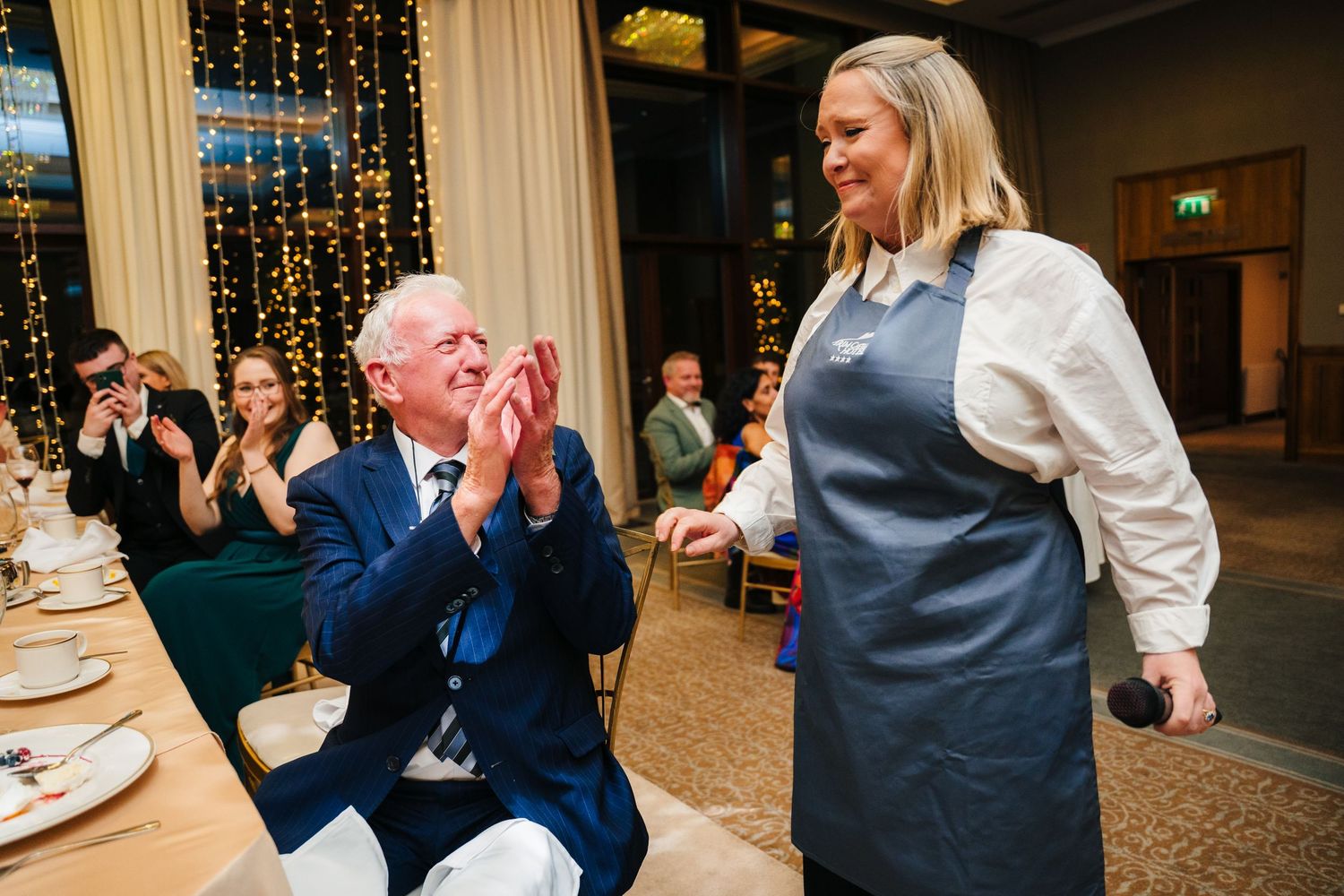 Wedding guests share an enthusiastic moment during the reception in a warmly lit venue with string lights.Wedding Photography Trim Castle Ir
