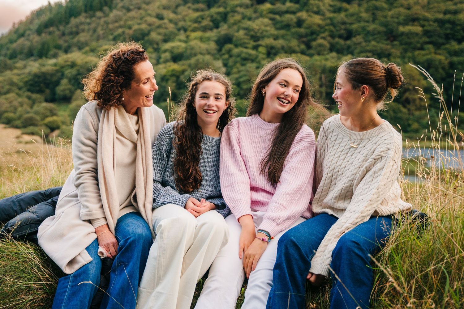 Family photographer Ireland Dublin Group sitting together on grassy hillside sharing laughs and conversation.