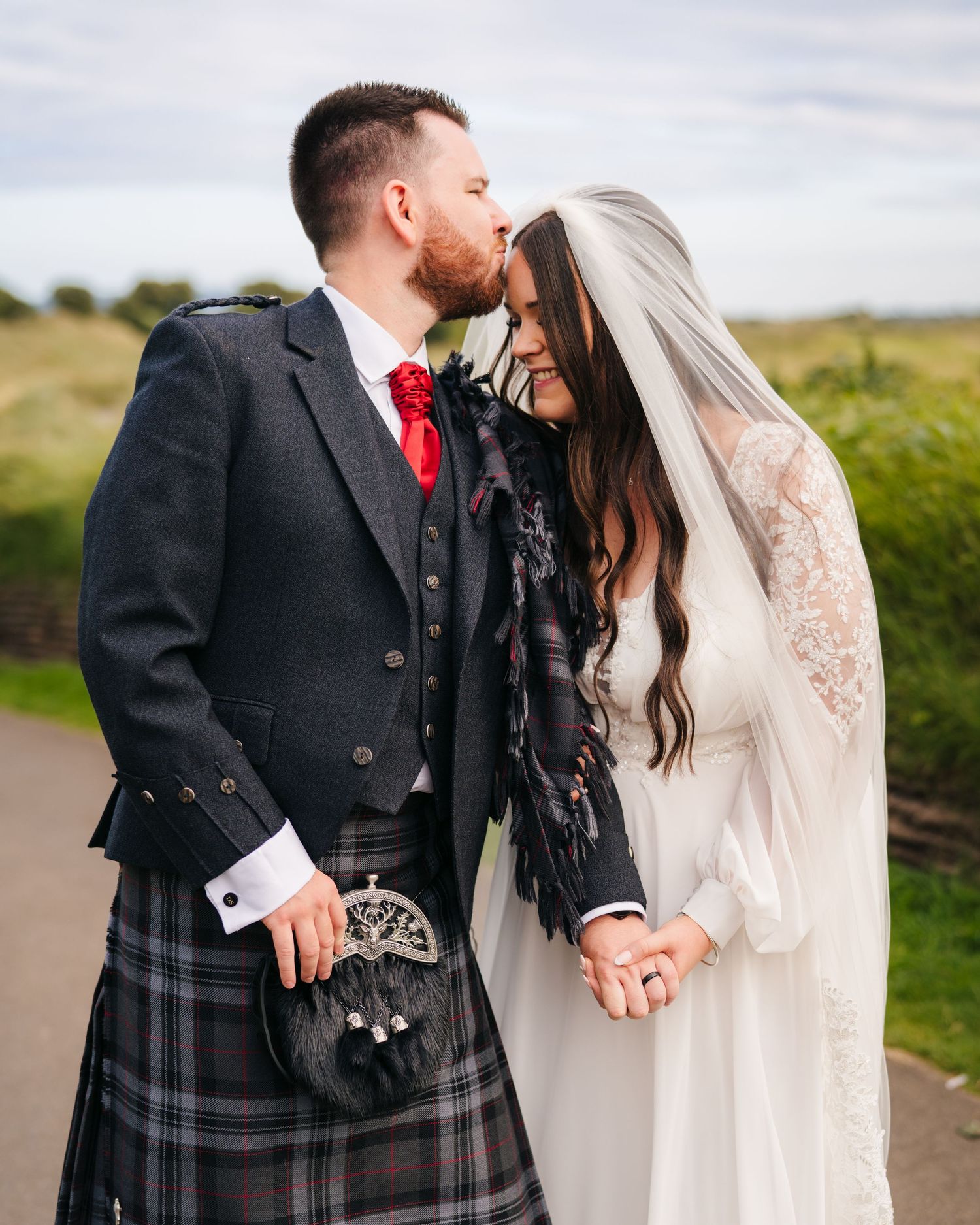 Traditional Scottish wedding attire with plaid kilts and white lace gown captured in detail. Portmarnock Hotel Wedding PHOTOGRAPHER Dublin