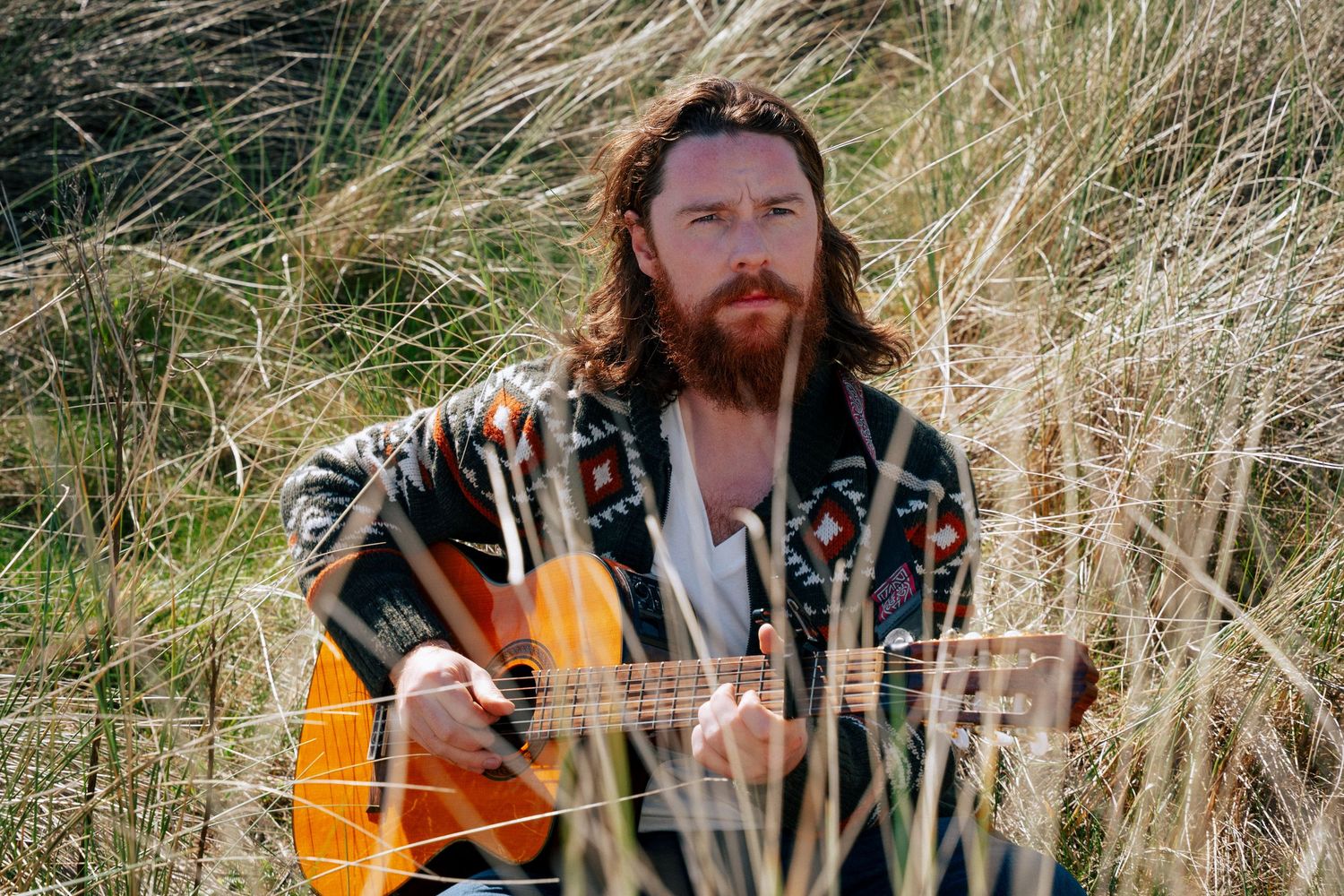 Acoustic guitarist playing among tall grass while wearing a floral print jacket. PHOTOGRAPHER Dublin
