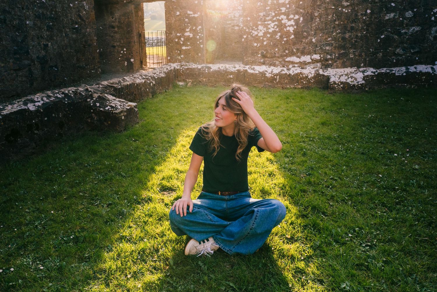 Person sitting cross-legged on grass in sunset light with stone ruins in background. Photographer Ireland dublin