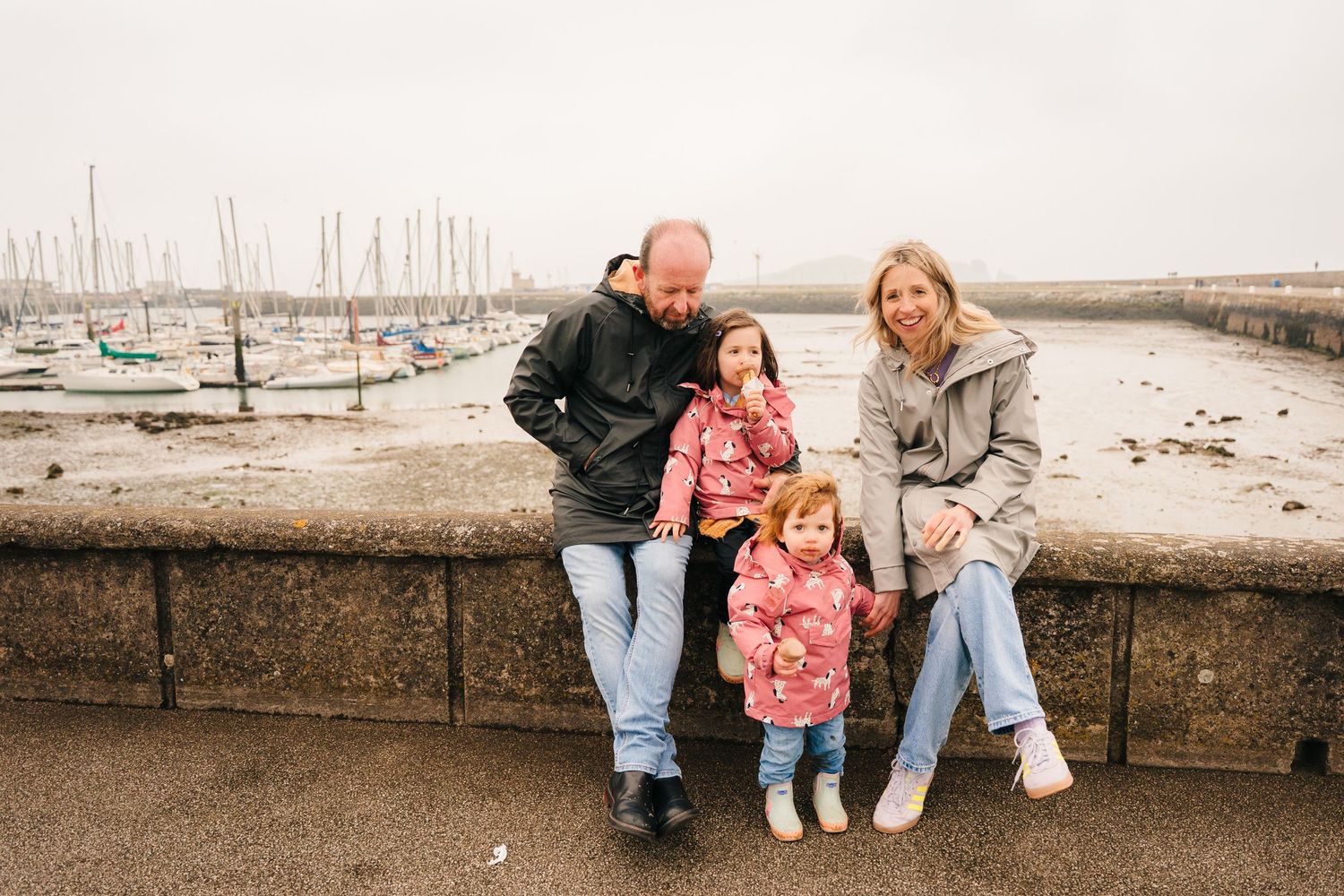 A family sits together on a stone wall overlooking a marina on an overcast day. PHOTOGRAPHER Dublin