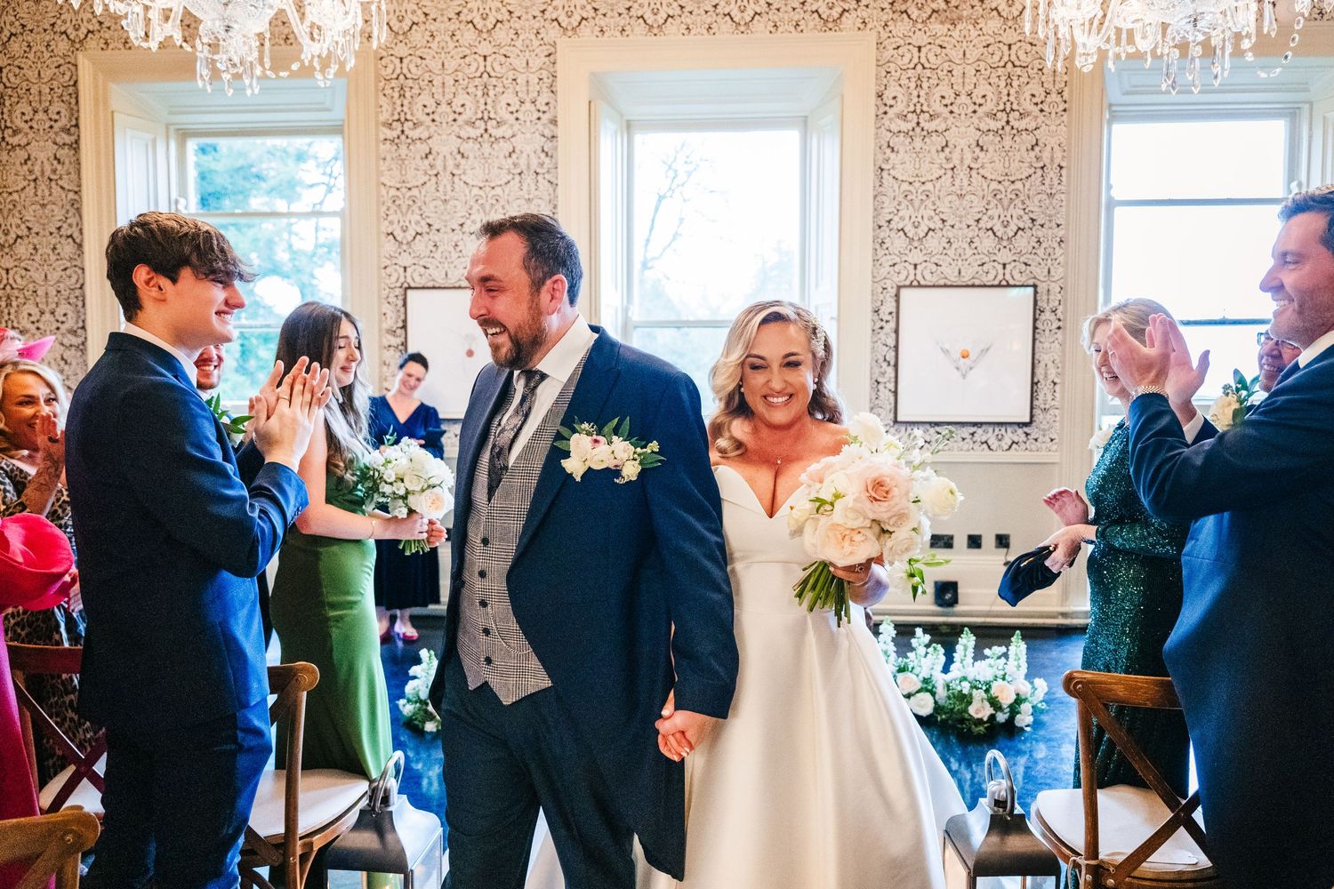 Wedding guests gather in an elegant room with decorative wallpaper and large windows for a celebration.  Virginia Park Lodge Wedding Photogr