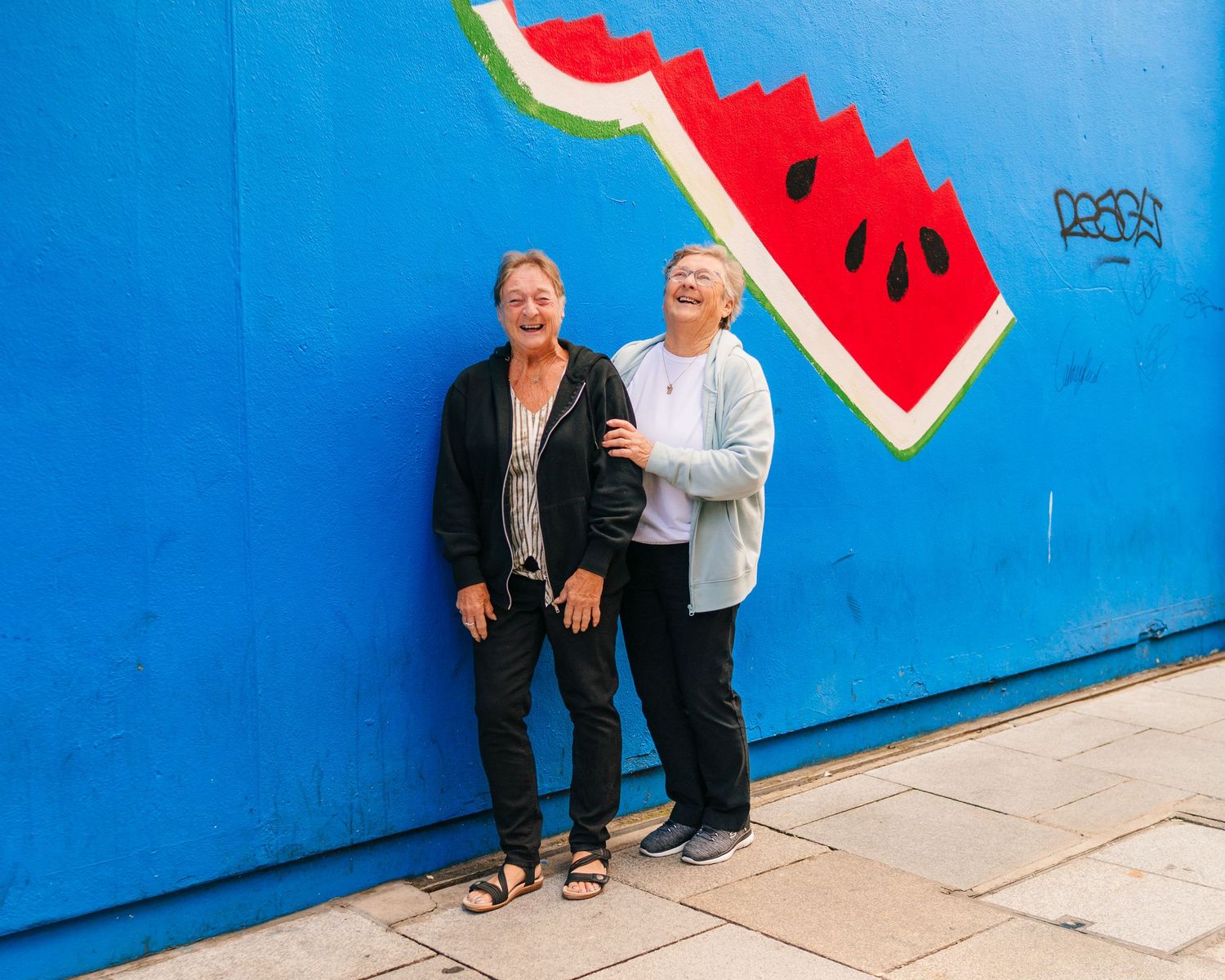 Two people standing against bright blue wall with painted watermelon slice street art. Family photographer Dublin Ireland