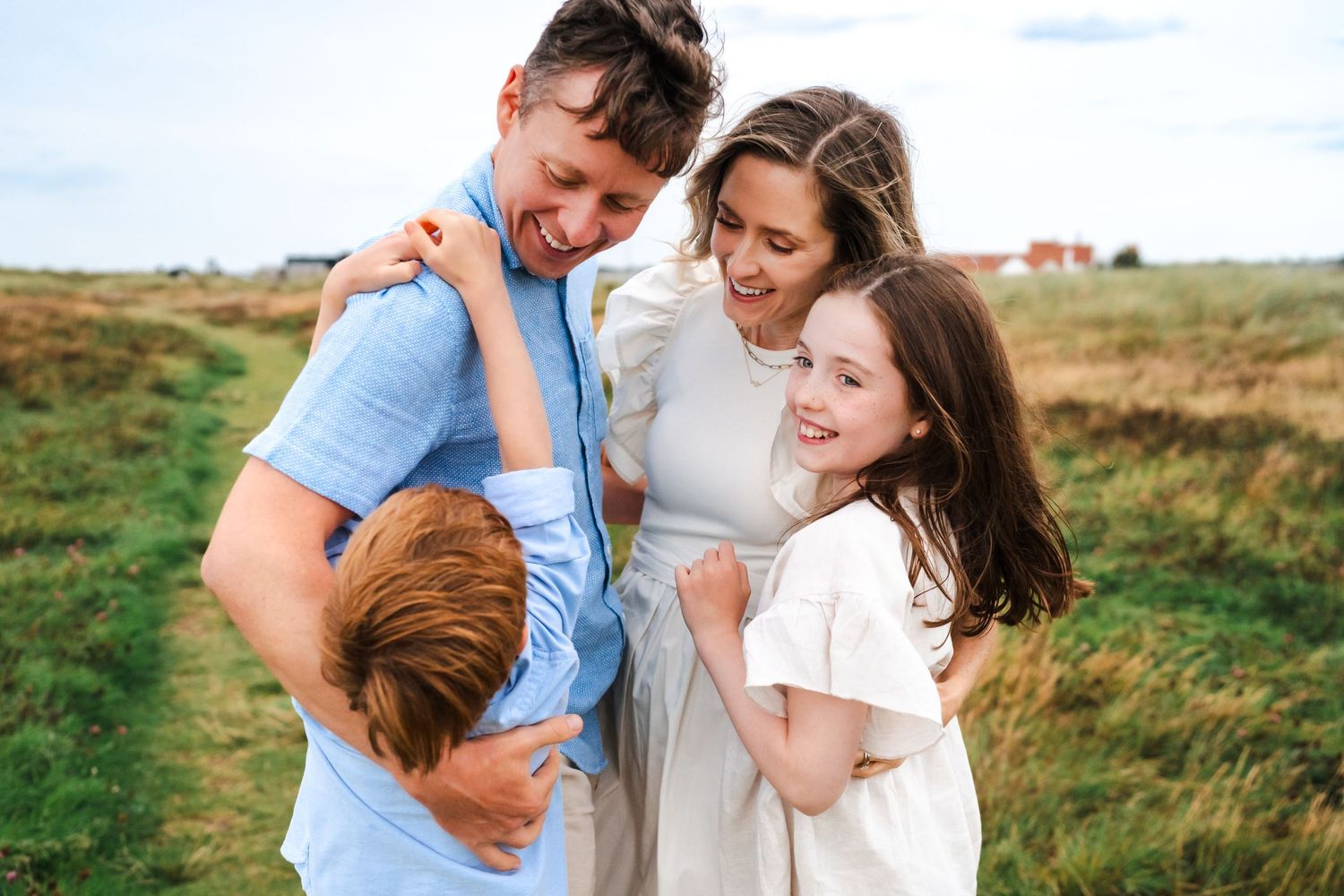 A family enjoys a tender moment together while walking along a grassy seaside path at sunset.  Family photographer Dublin Ireland