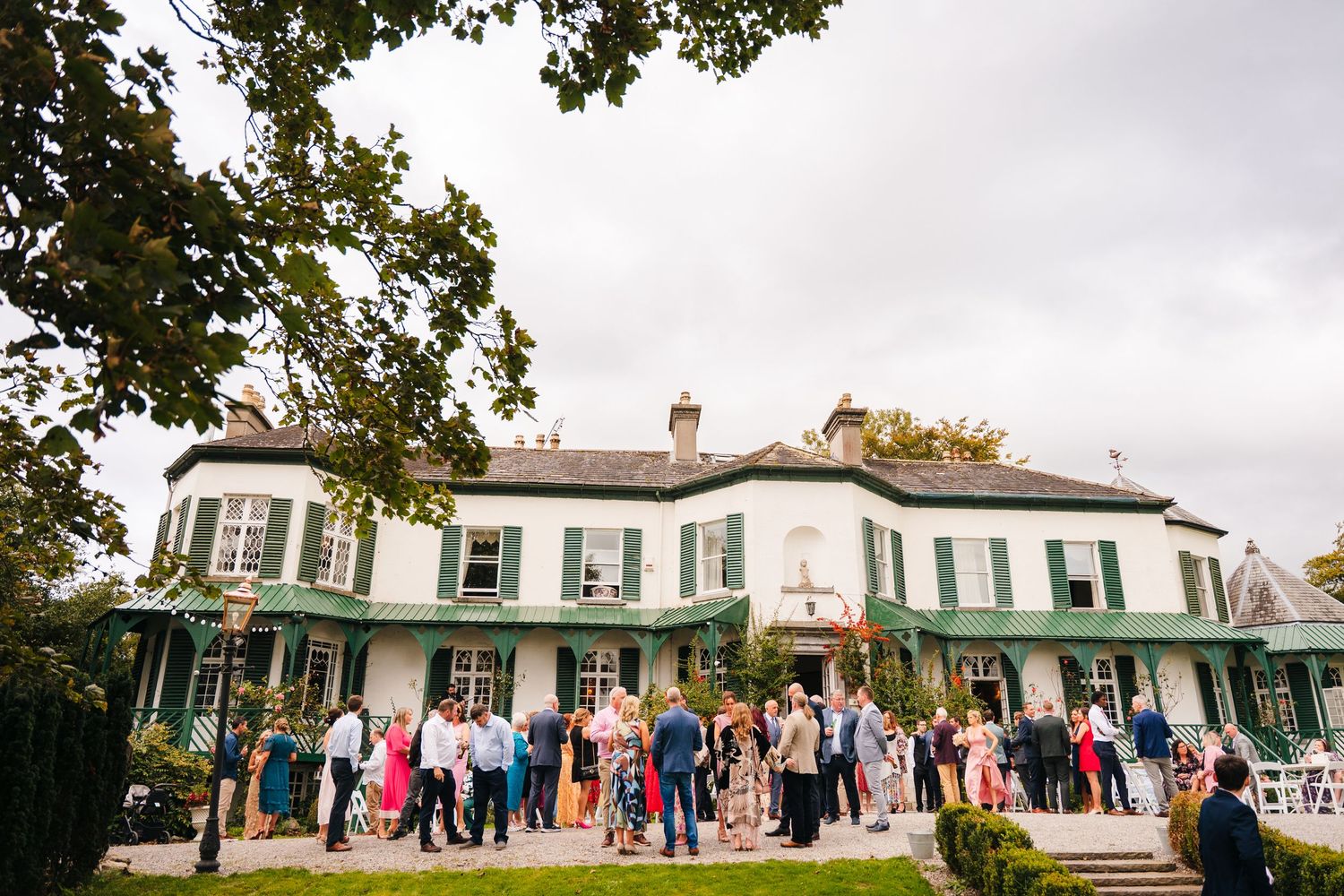 Wide shot of a classic white colonial house with guests gathered outside for an event. LGBTQ Ashley Park Wedding Photographer