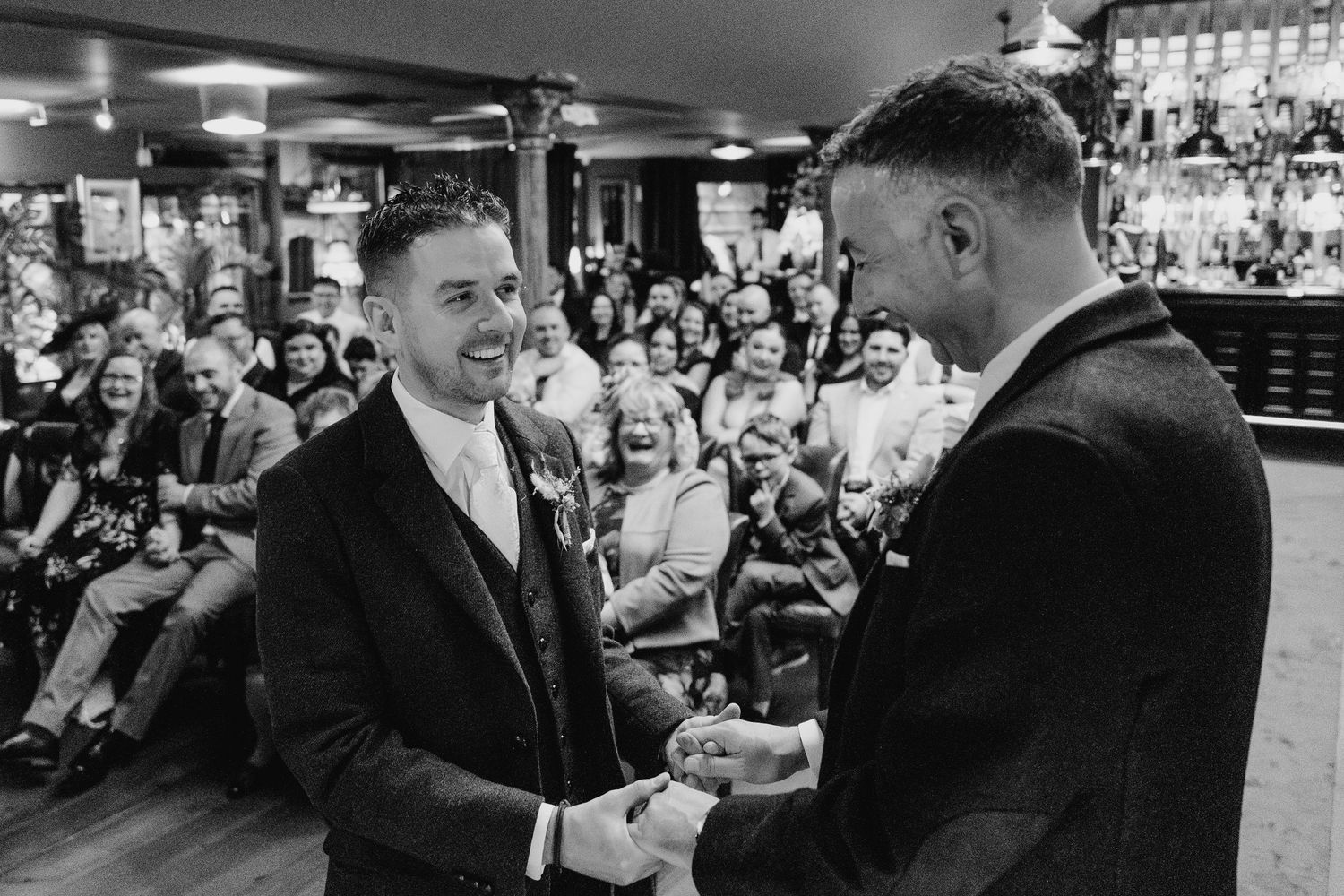 Black and white photo of guests enjoying drinks and conversation at a wedding bar.