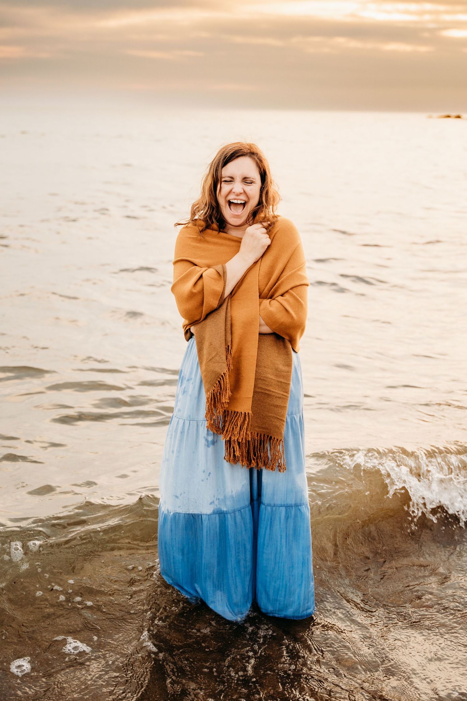 Person wearing mustard colored cardigan and blue ombre maxi dress stands joyfully at the beach during sunset. PHOTOGRAPHER Dublin ireland