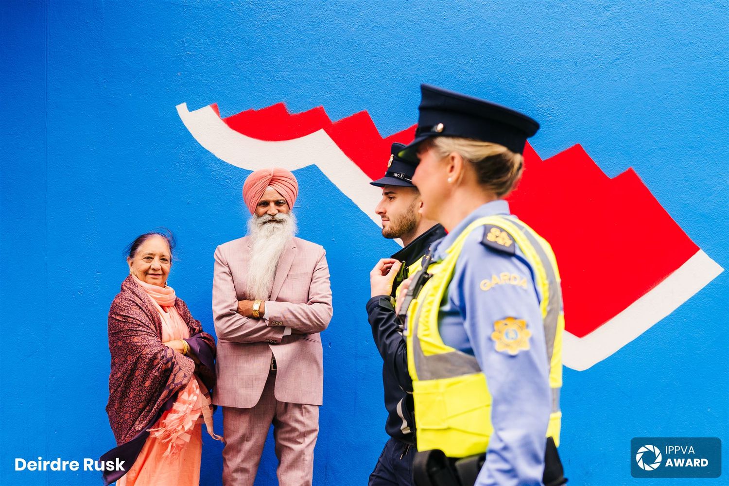 Police officer stands near people against vibrant red and white wall art outdoors. Family PHOTOGRAPHER Dublin PHOTOGRAPHER Dublin
