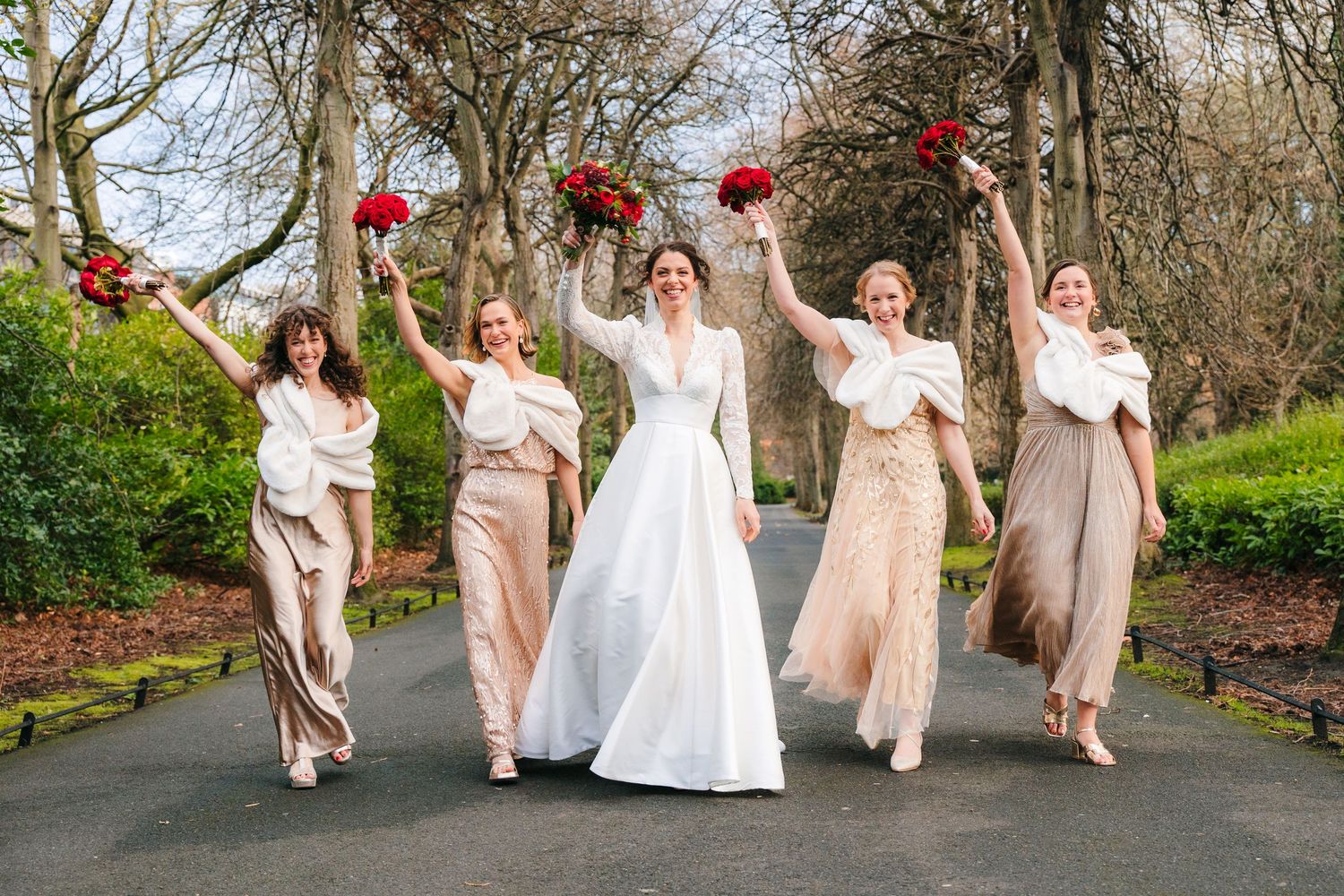 Bridesmaids in blush pink dresses jump playfully outside in a garden setting with red floral accents. Stephens green club dublin Wedding pho