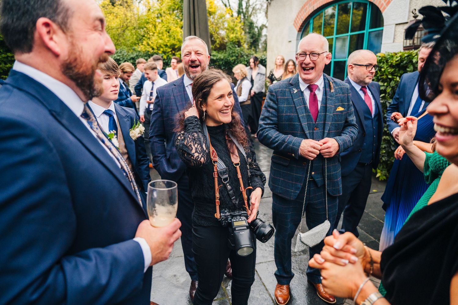 A group of wedding guests share laughter and conversation during an outdoor cocktail reception. Wedding photographer Dublin