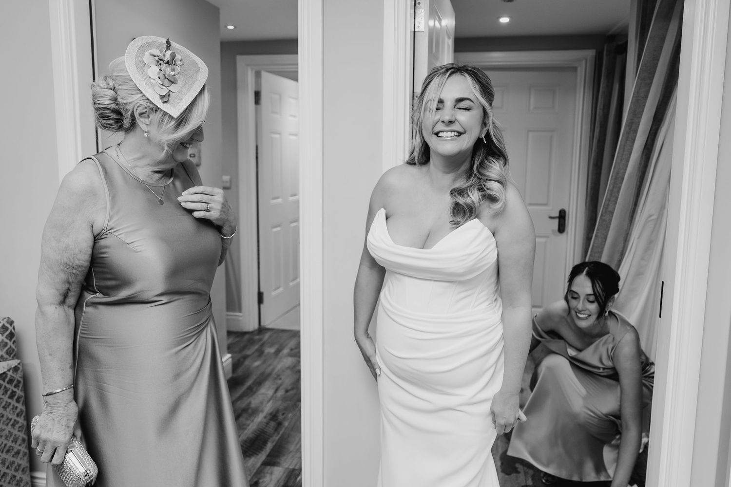 Bride in white off-shoulder gown laughs with bridesmaids in satin dresses during wedding preparations. Wedding photographer Dublin