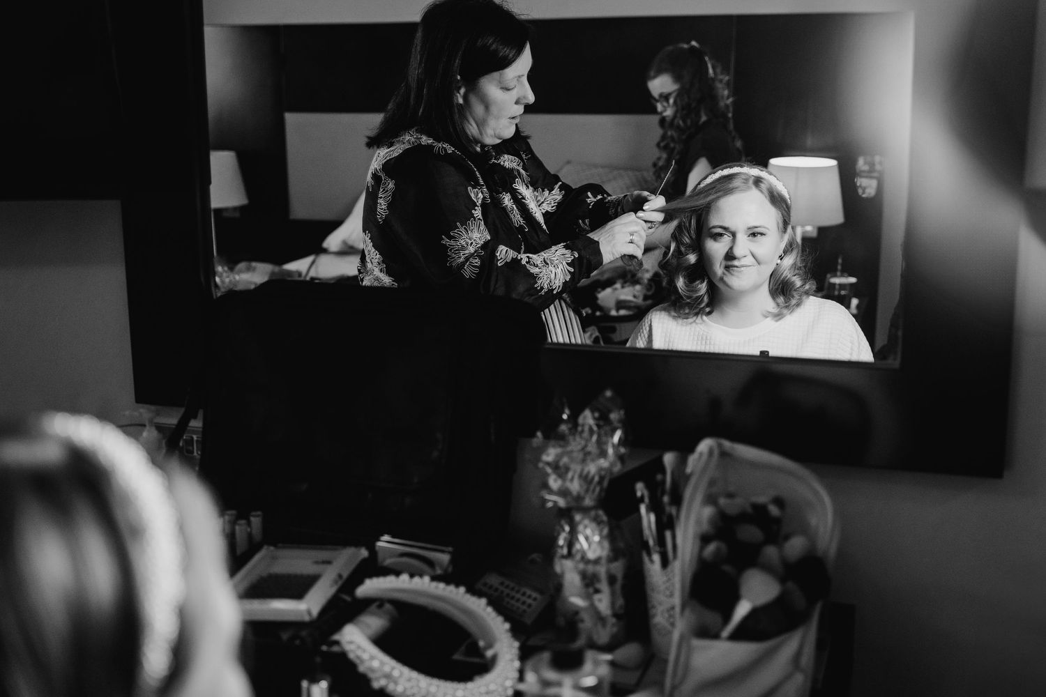 A black and white image showing someone getting their hair and makeup done at a vanity mirror.  Wedding PHOTOGRAPHER Trim Castle