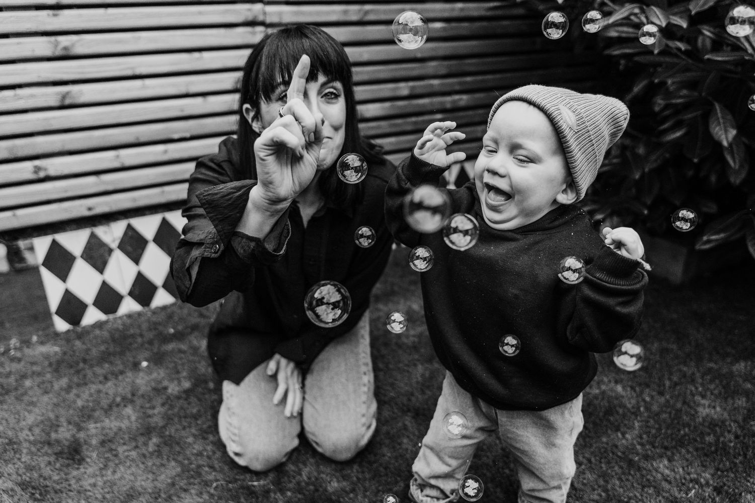 Black and white candid family photos showing children playing with bubbles against wooden fence background.  Family PHOTOGRAPHER Dublin