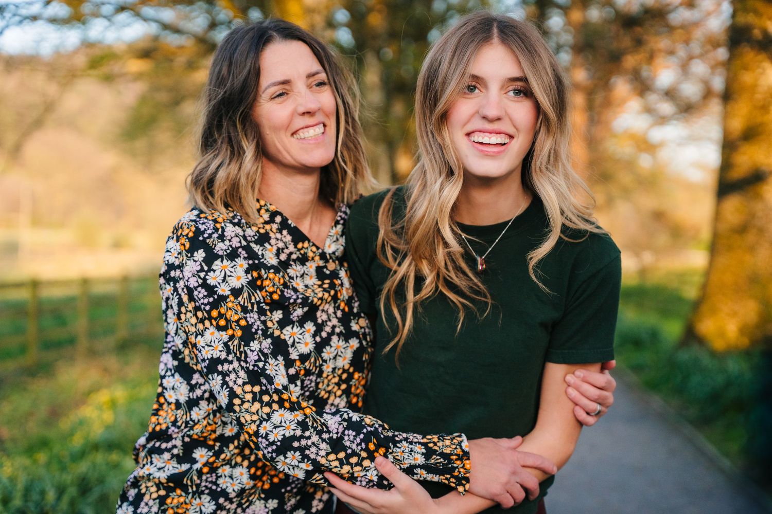 Two women wearing fall outfits embrace and laugh together on an outdoor path during golden hour at sunset. Photographer Ireland dublin