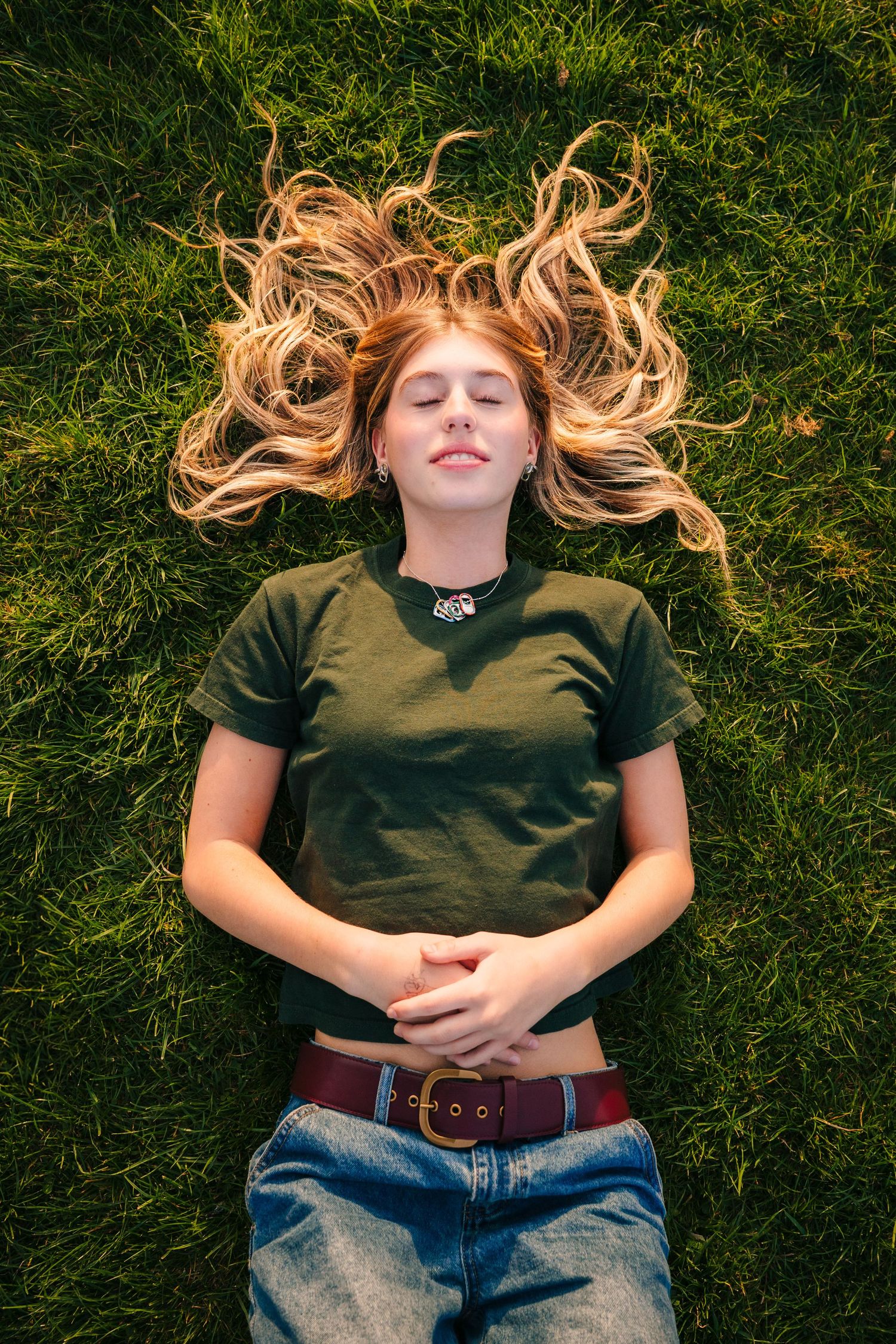 Woman with flowing blonde hair lying on green grass wearing casual attire. Photographer Ireland dublin