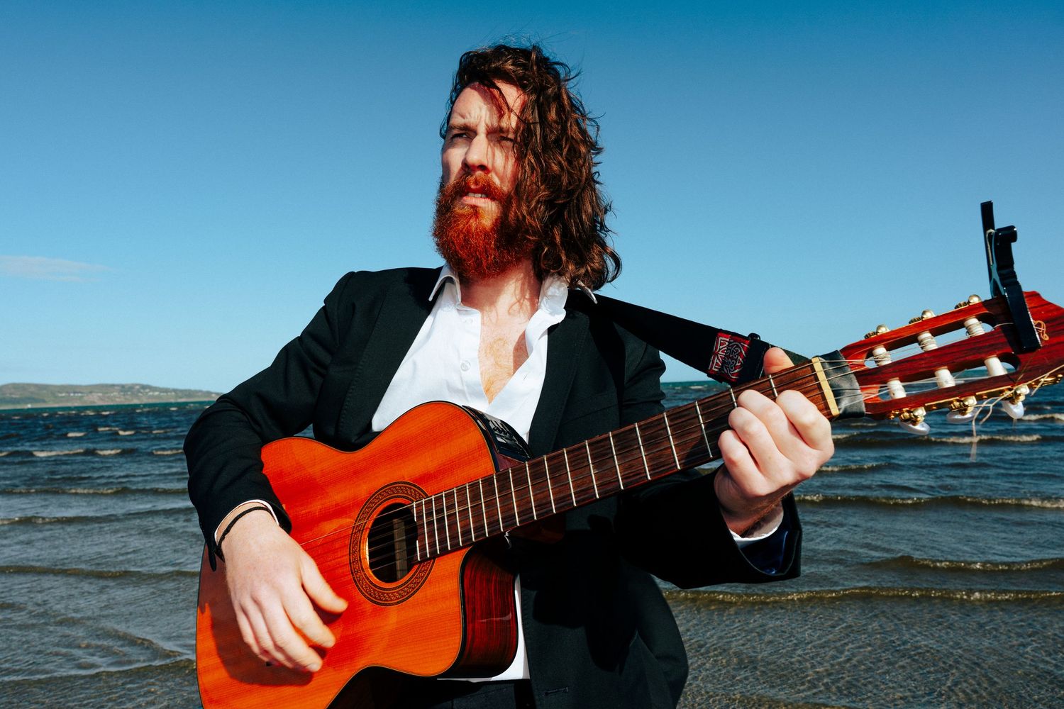 Guitarist performing with acoustic guitar by the water on a bright sunny day. PHOTOGRAPHER Dublin