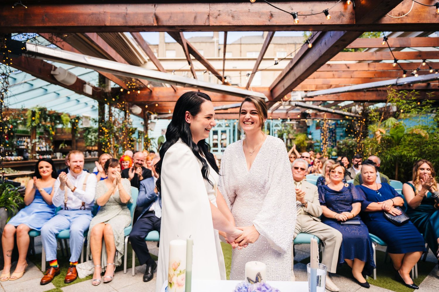 A wedding ceremony taking place under a wooden pergola with guests seated in rows. House Dublin Wedding Photographer