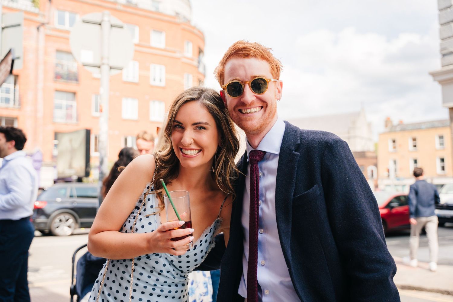 Pair posing together at outdoor gathering with orange brick building in background. Same sex wedding PHOTOGRAPHER Dublin