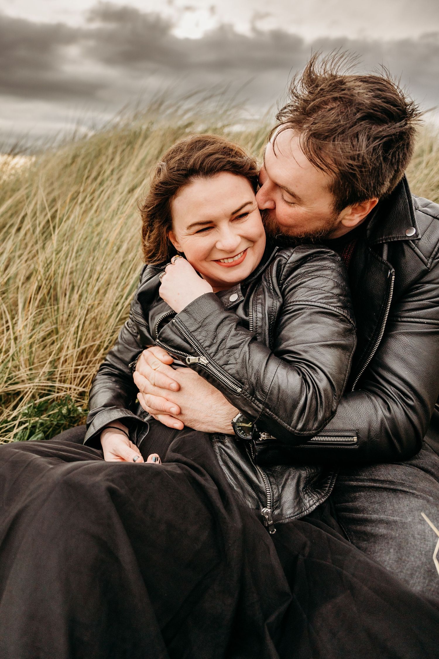 Intimate beach portrait with sea grass swaying in the wind under cloudy skies. engagement PHOTOGRAPHER Dublin