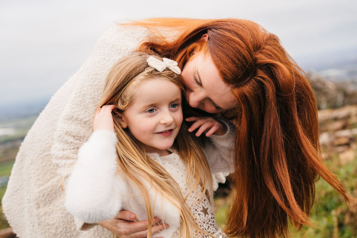 Family Photographer Dublin Ireland A tender moment shared between two people wrapped in a cream blanket against a scenic mountain backdrop.
