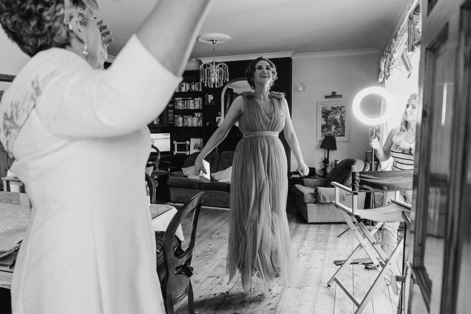 Black and white photo showing people in elegant dresses getting ready in a room with bookshelves and decor. Millhouse slane wedding photogra