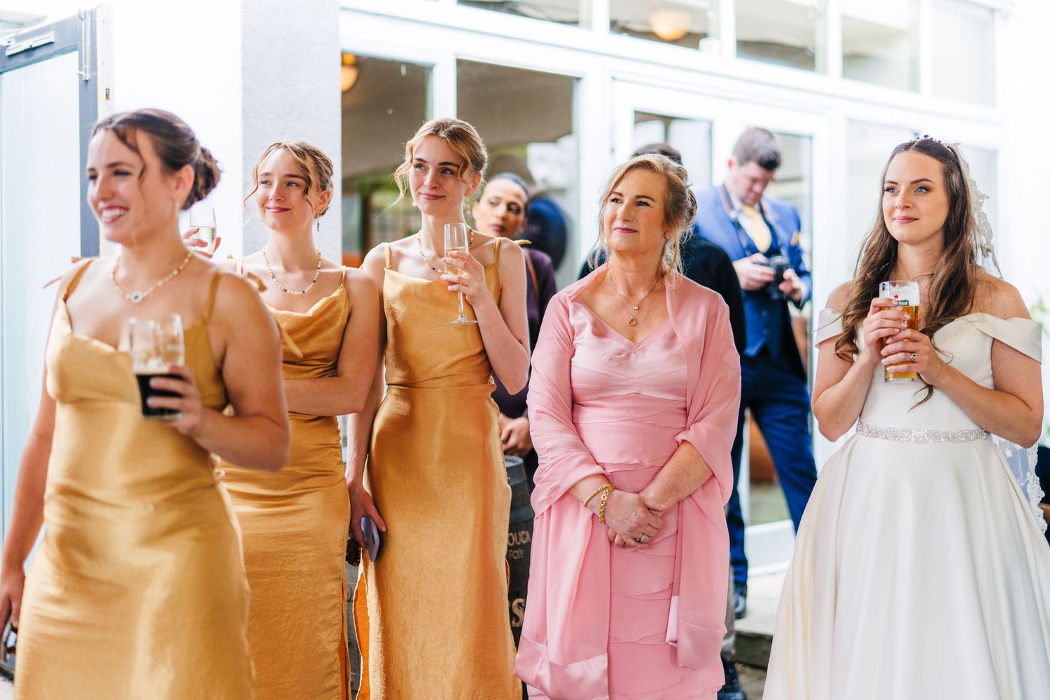 Poulaphouca Wedding photographeWedding party members in gold dresses and white gown stand together sharing candid laughs during celebration.