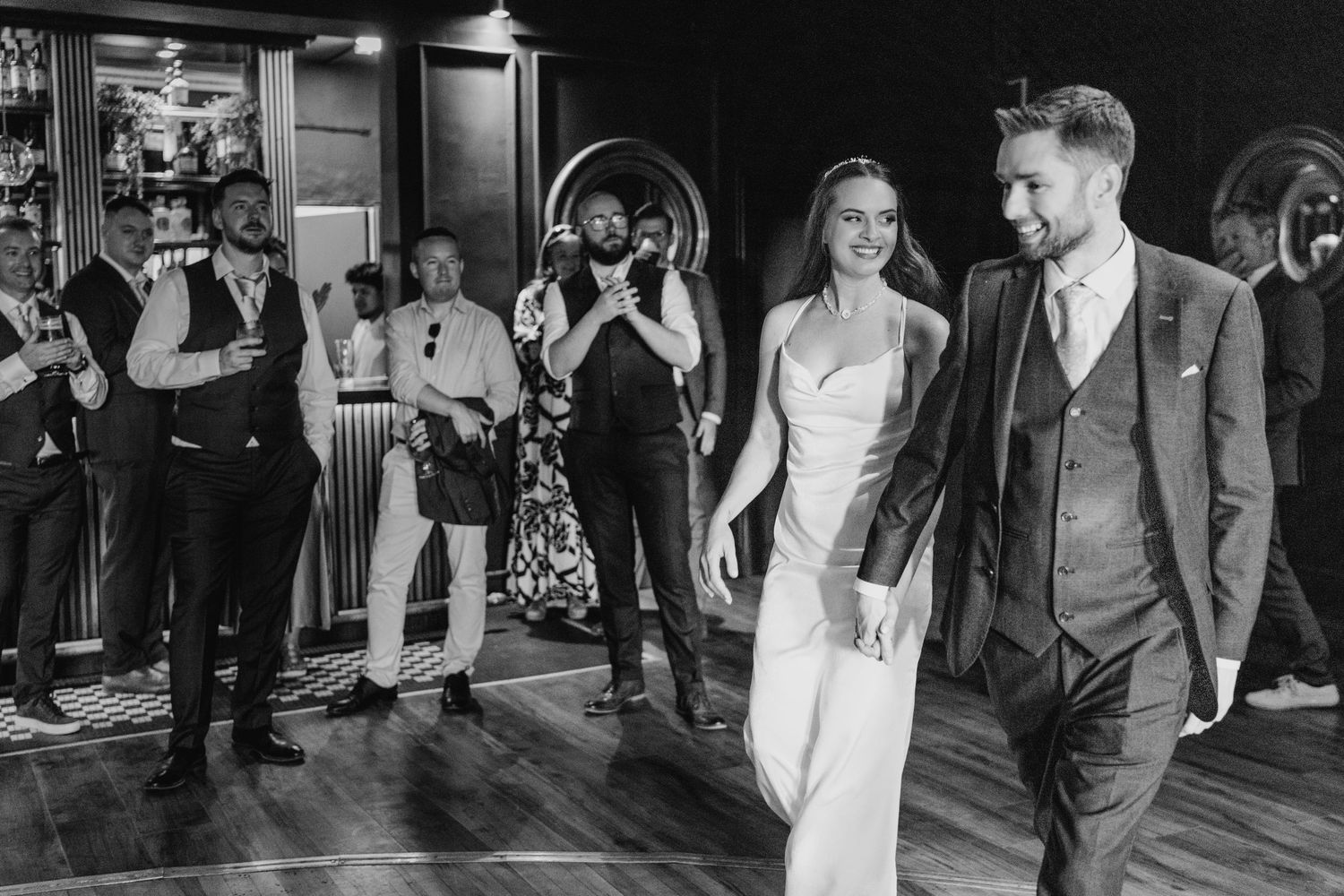 Poulaphouca Wedding photographer wickBlack and white photo of a wedding celebration with guests clapping as couple walks across dance floor.