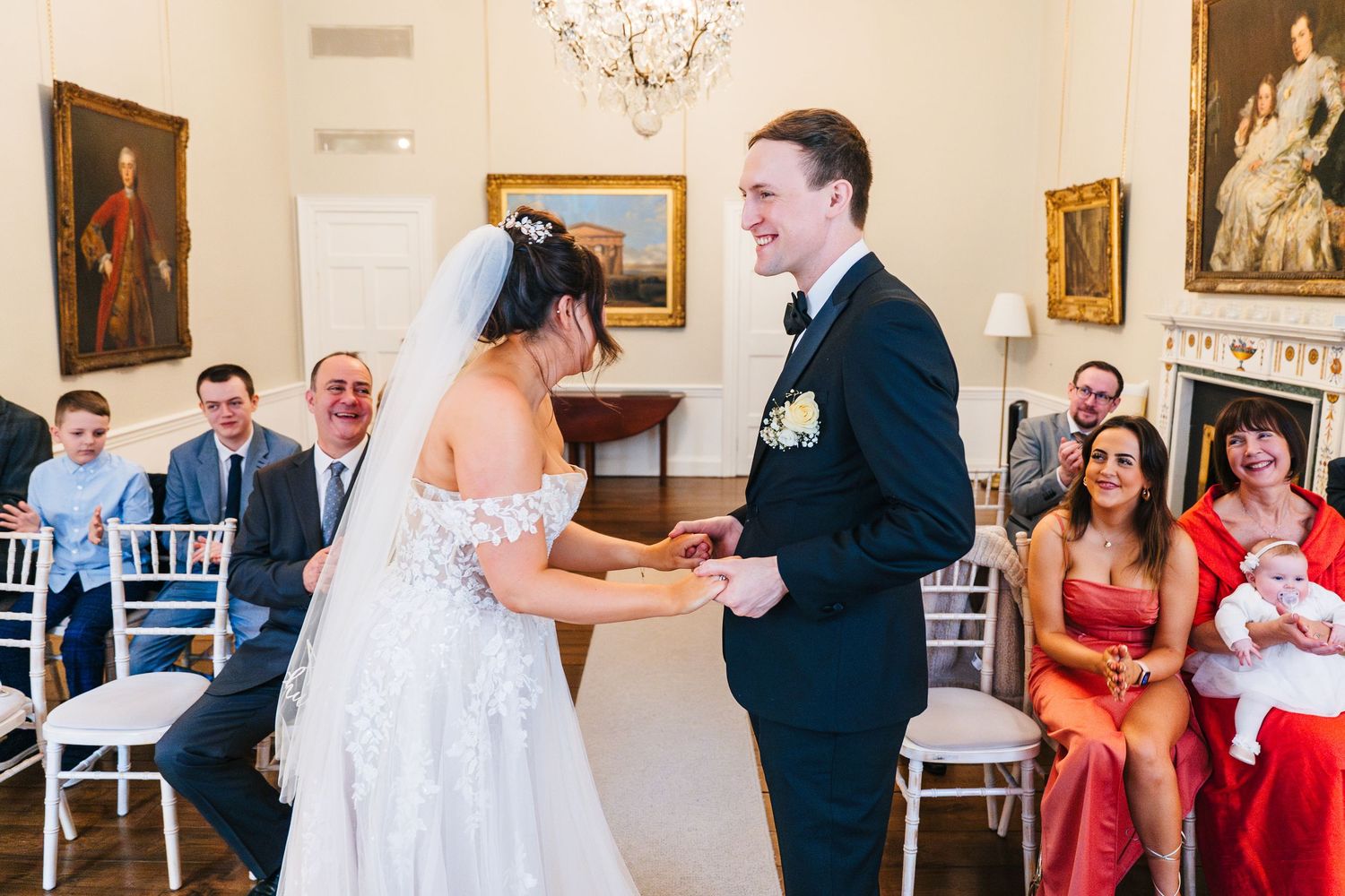 Joyful wedding ceremony moment in an elegant room with vintage paintings and white chairs. Wedding PHOTOGRAPHER Dublin