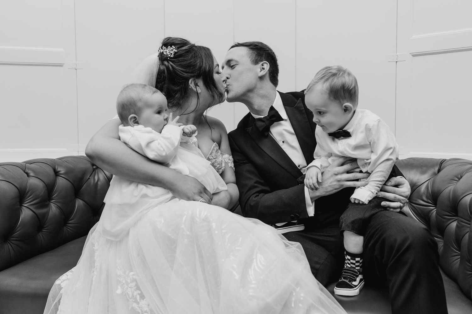 An intimate black and white moment of a wedding couple on a leather couch with two small children. Wedding PHOTOGRAPHER Dublin